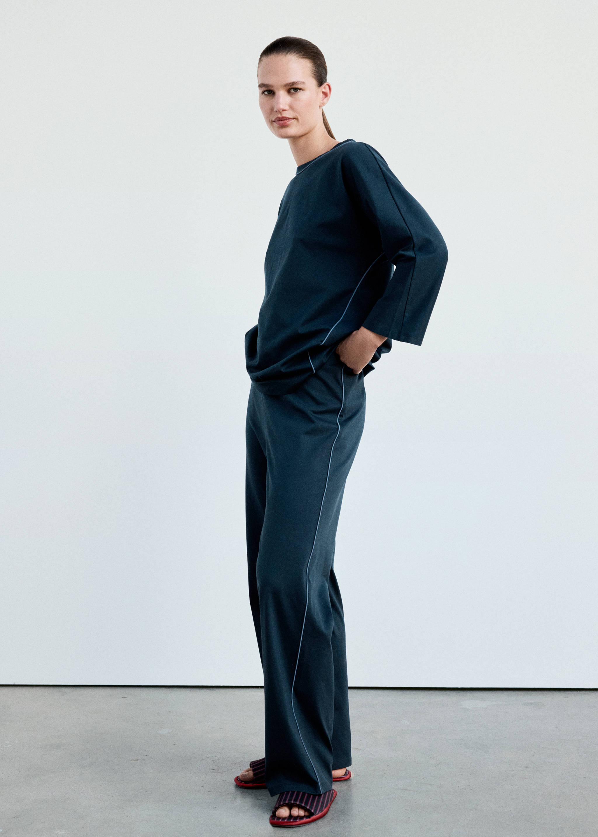 Dark teal pyjama trousers with white piping, worn with a matching top.