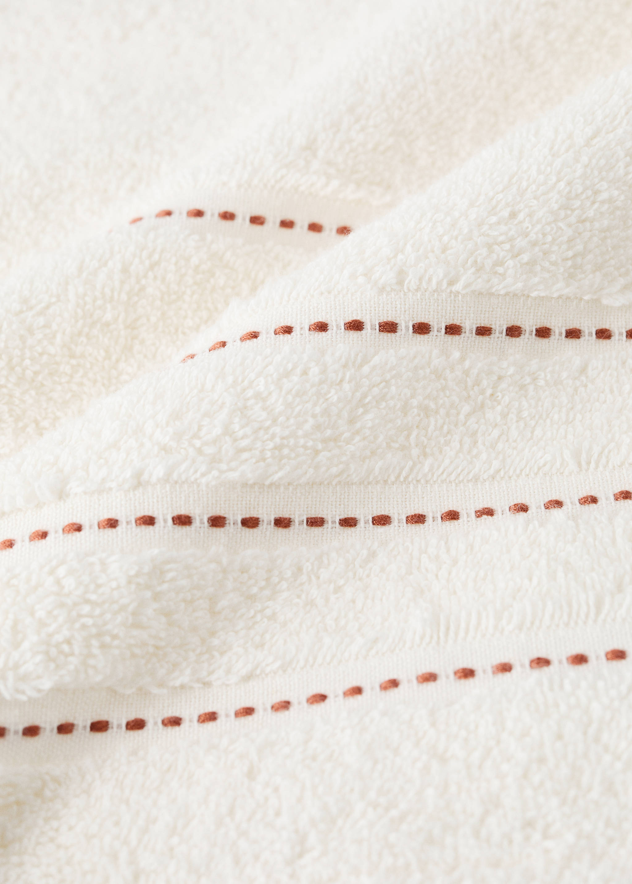 Close-up of a cream towel with woven brown dashed stripes.