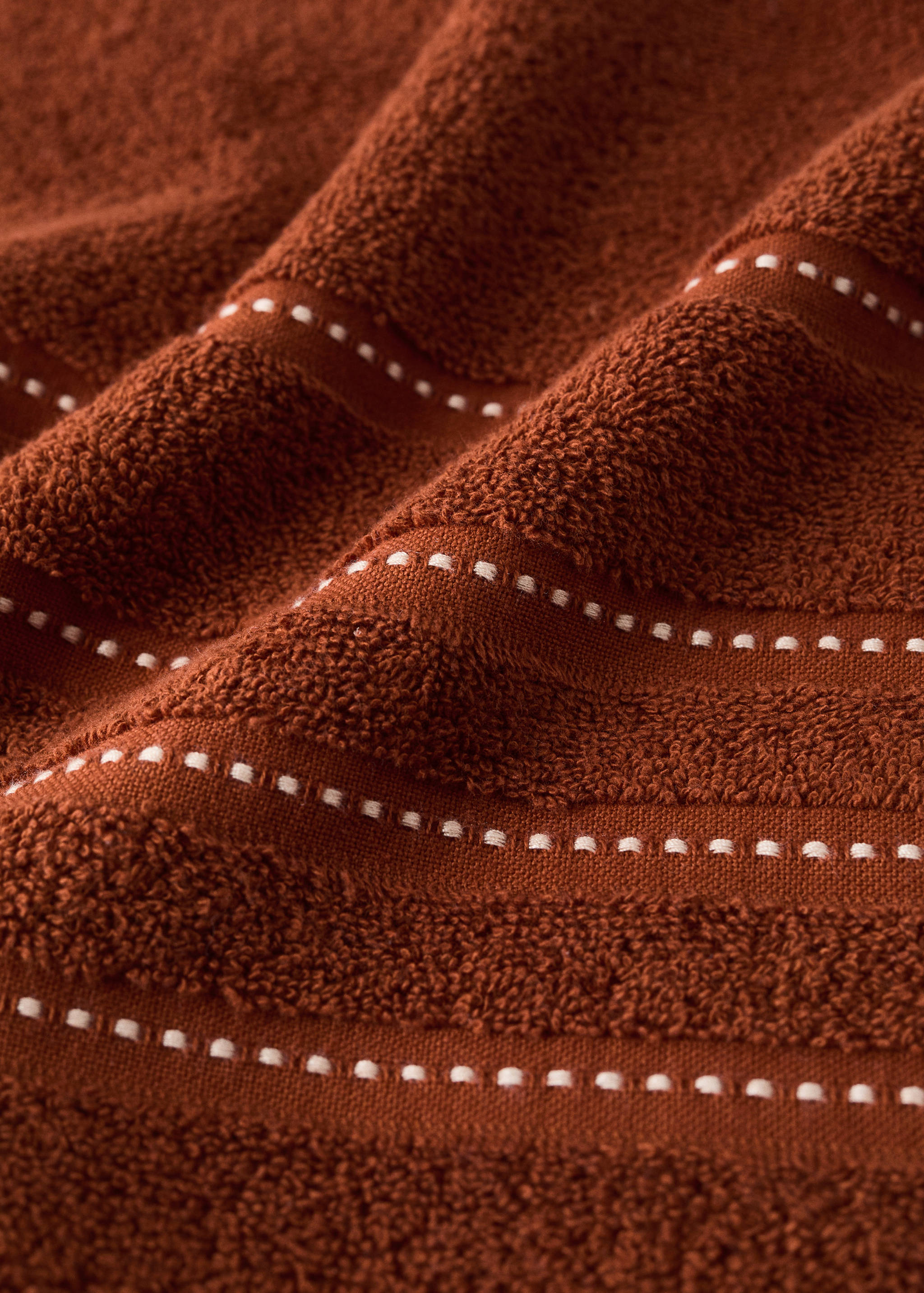 Rust-orange towel close-up showing textured fabric and woven striped details.
