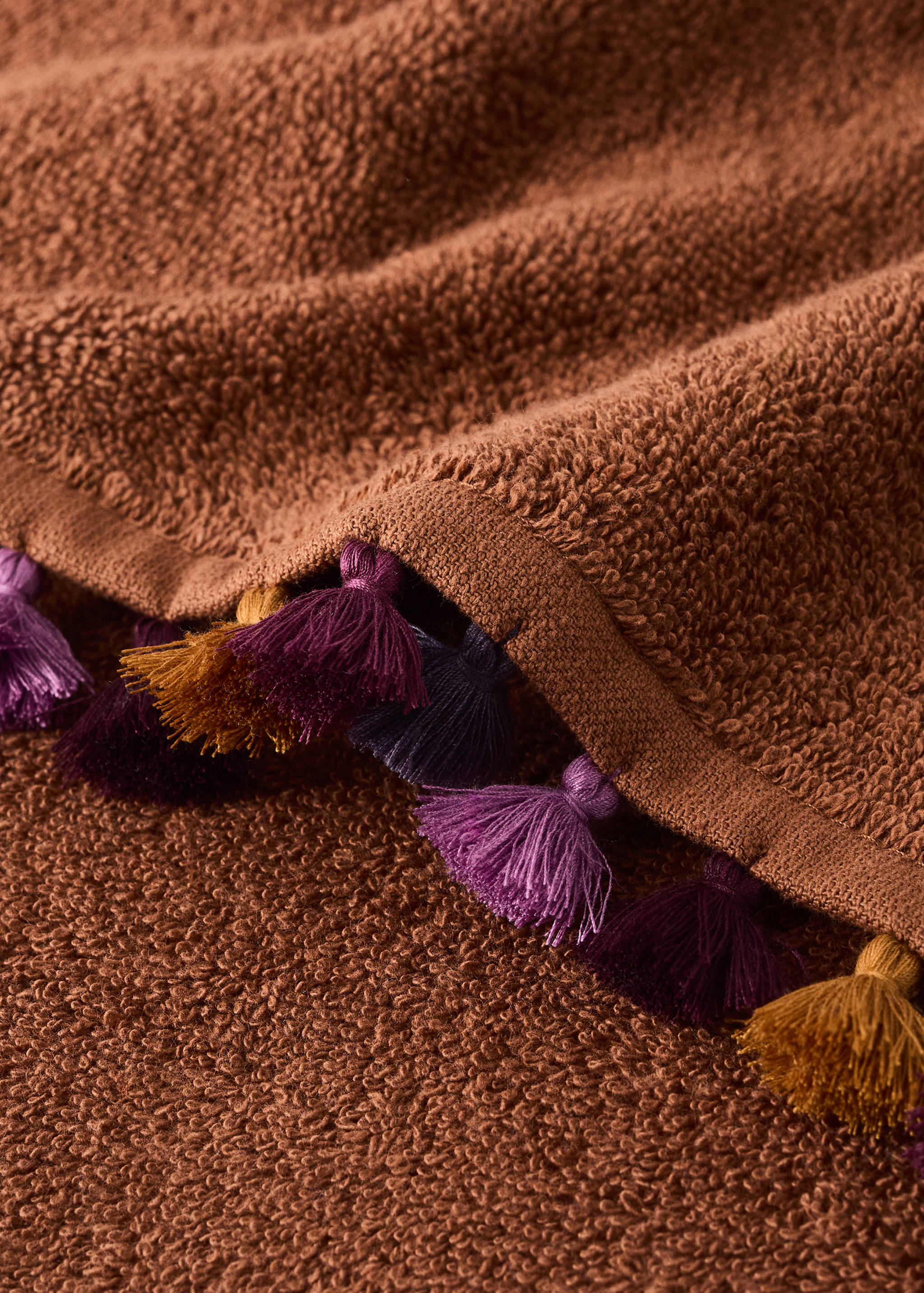 Terracotta towel with textured weave and colourful tassel trim.