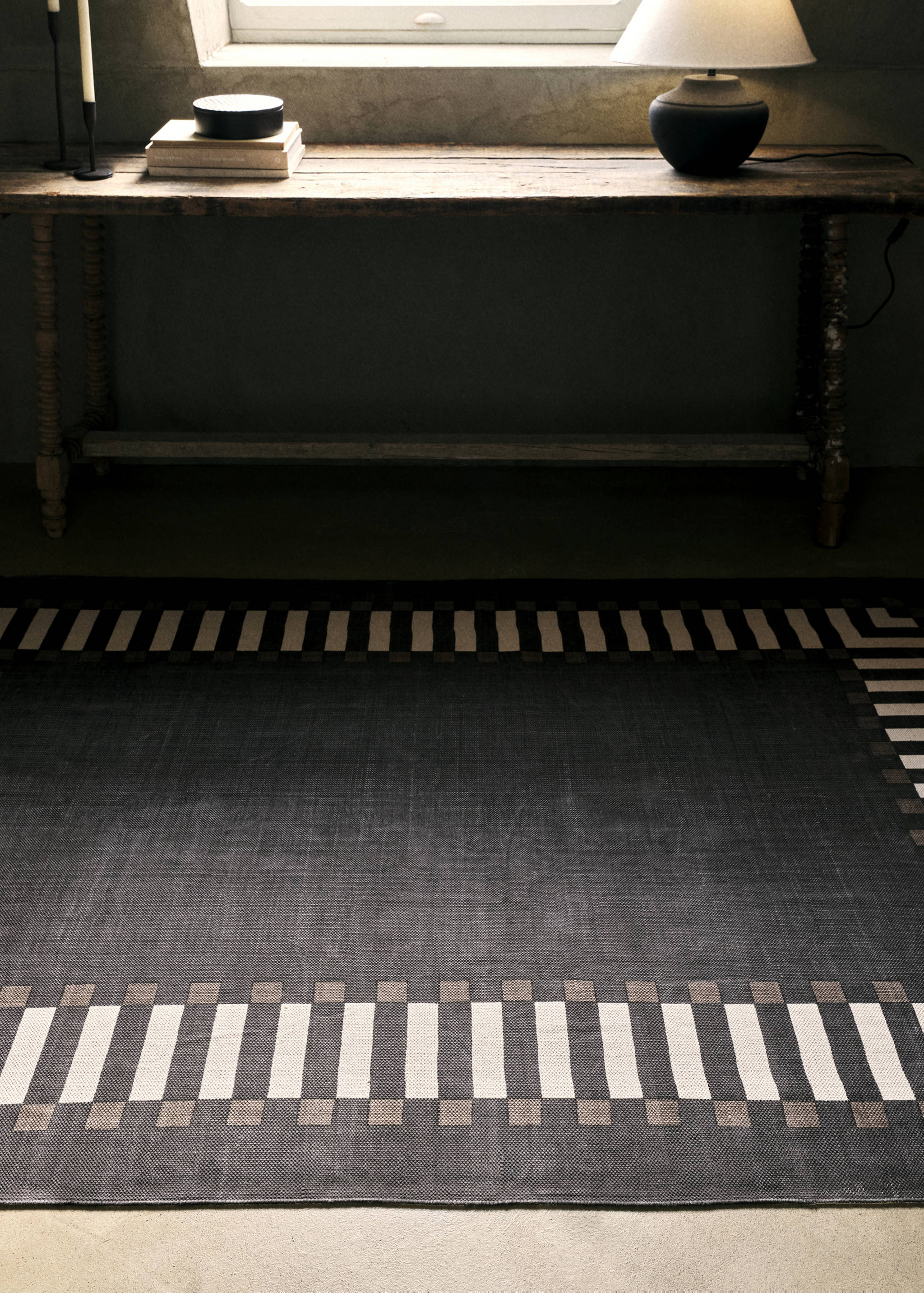 Dark grey woven rug with a contrasting white and neutral block-patterned border.