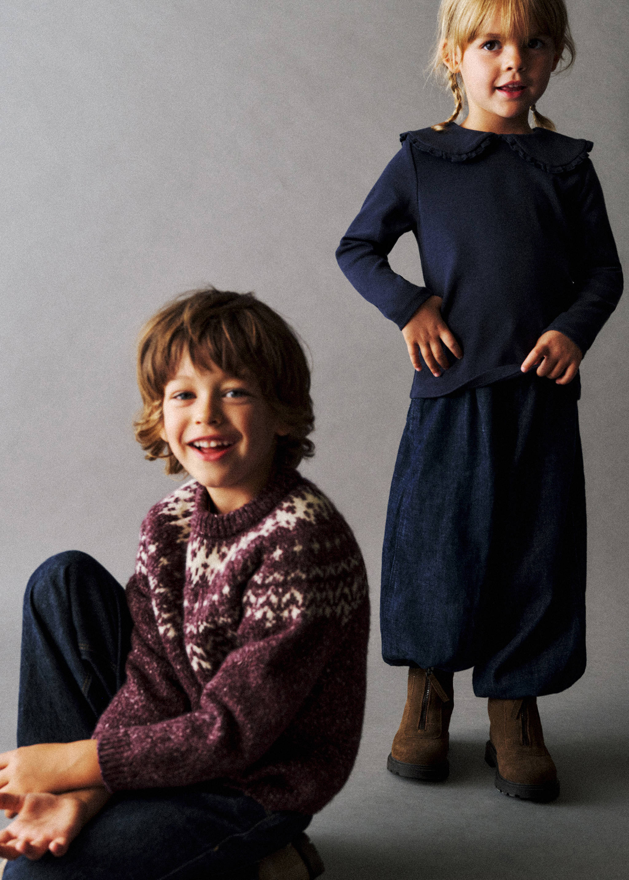 Dark blue long-sleeved t-shirt with a ruffled collar, worn by a standing girl next to a boy in a knitted jumper.