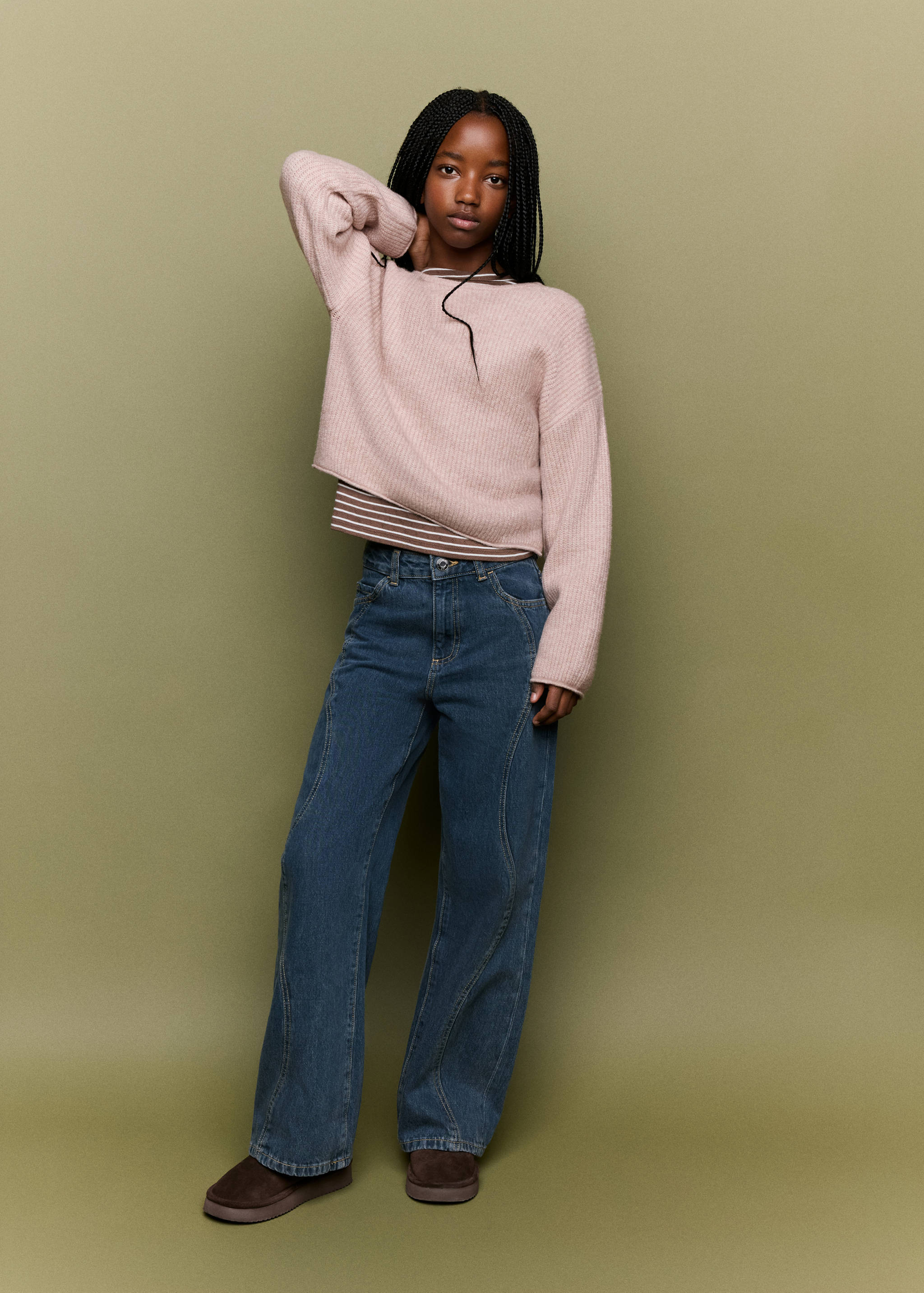 Pink relaxed-fit knit jersey layered over a striped top, with blue trousers.