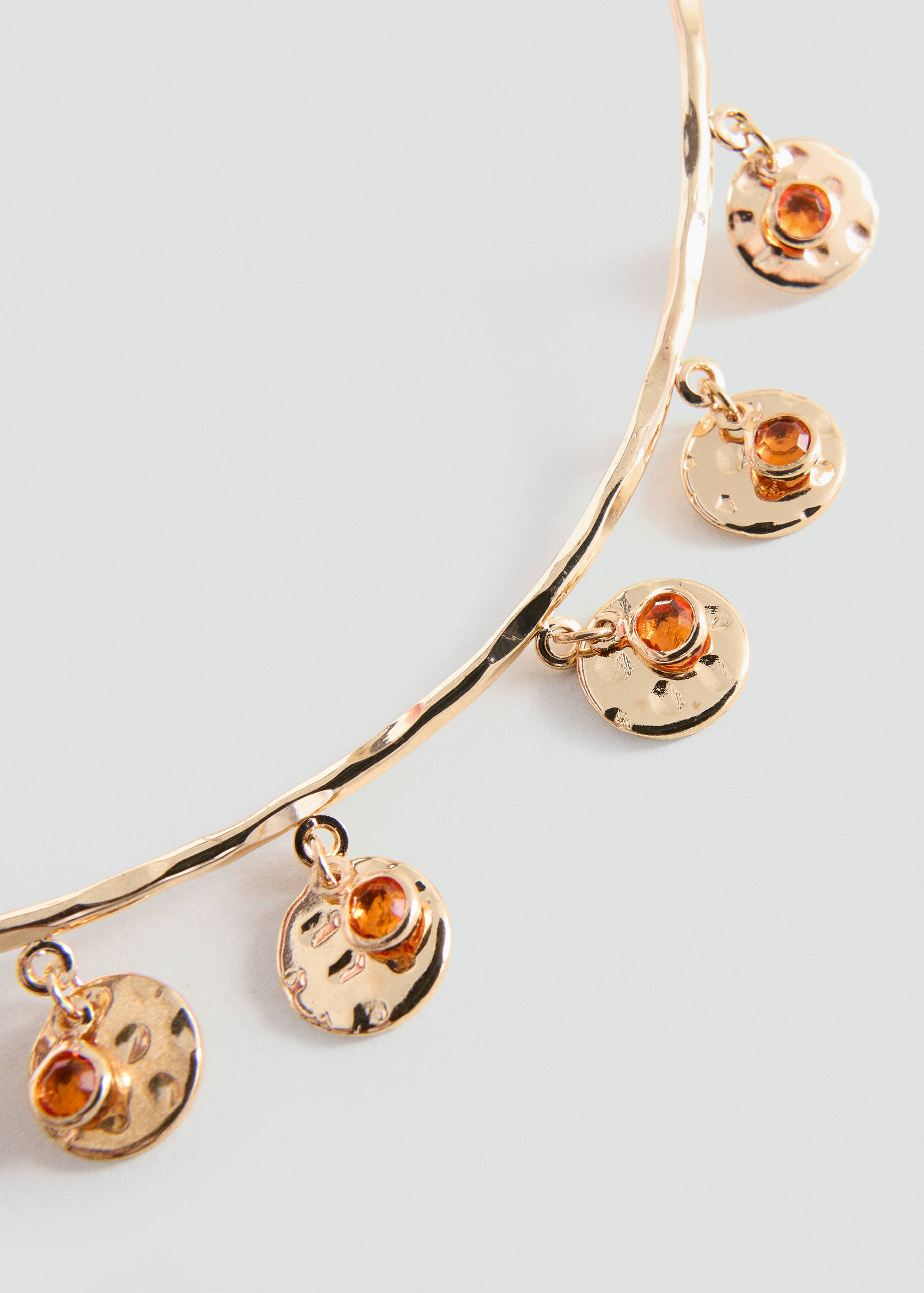 Gold-coloured hammered collar necklace with dangling coin charms set with orange crystals.