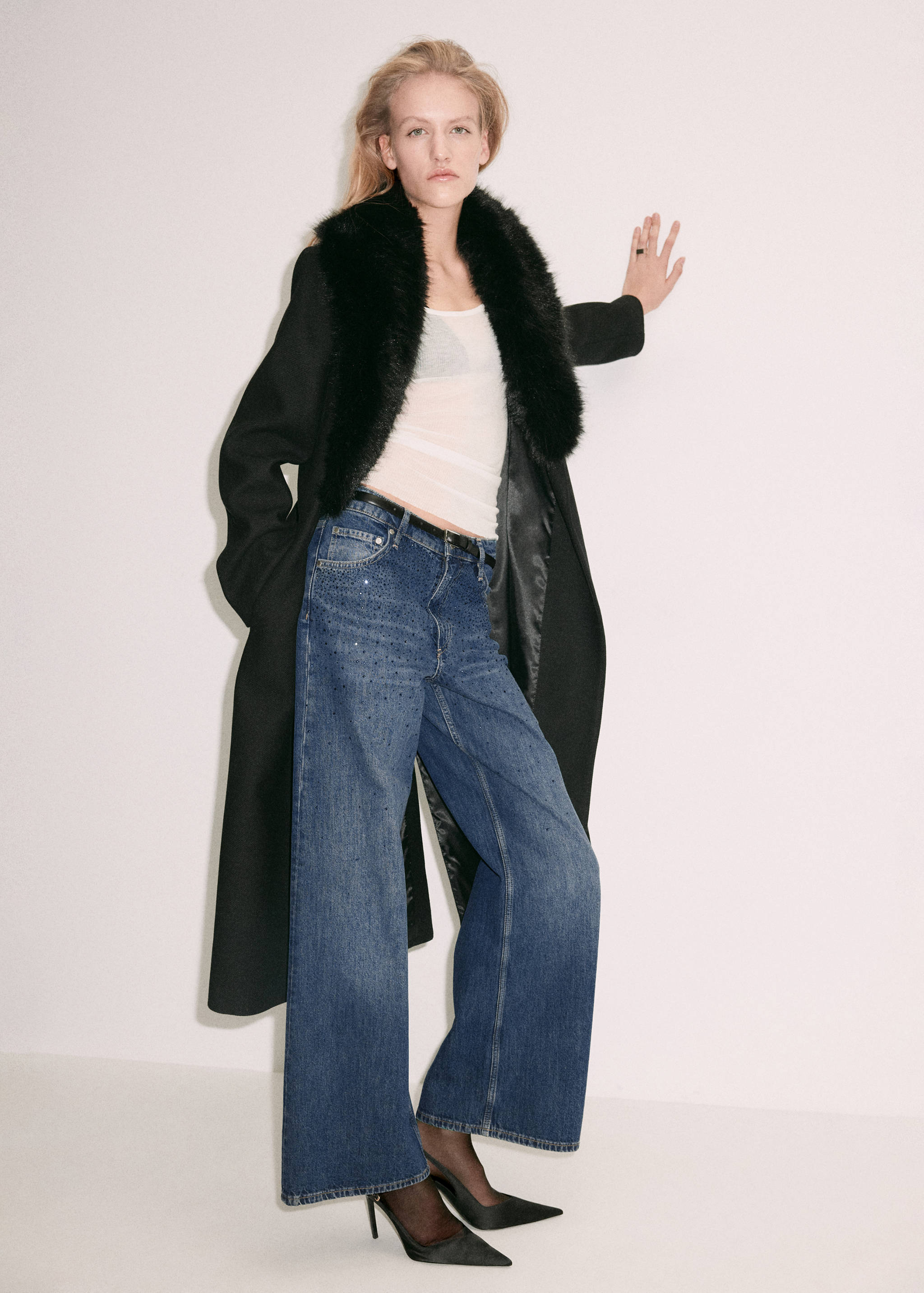 Blue embellished wide-leg denim trousers worn with a black coat and faux-fur collar.