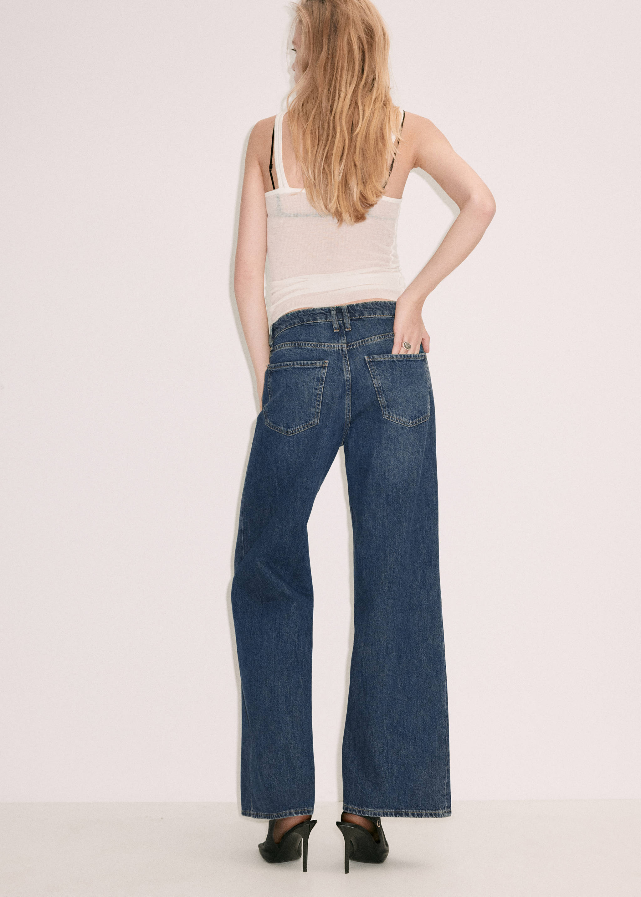 Back view of blue denim trousers with a low waist and back pockets.