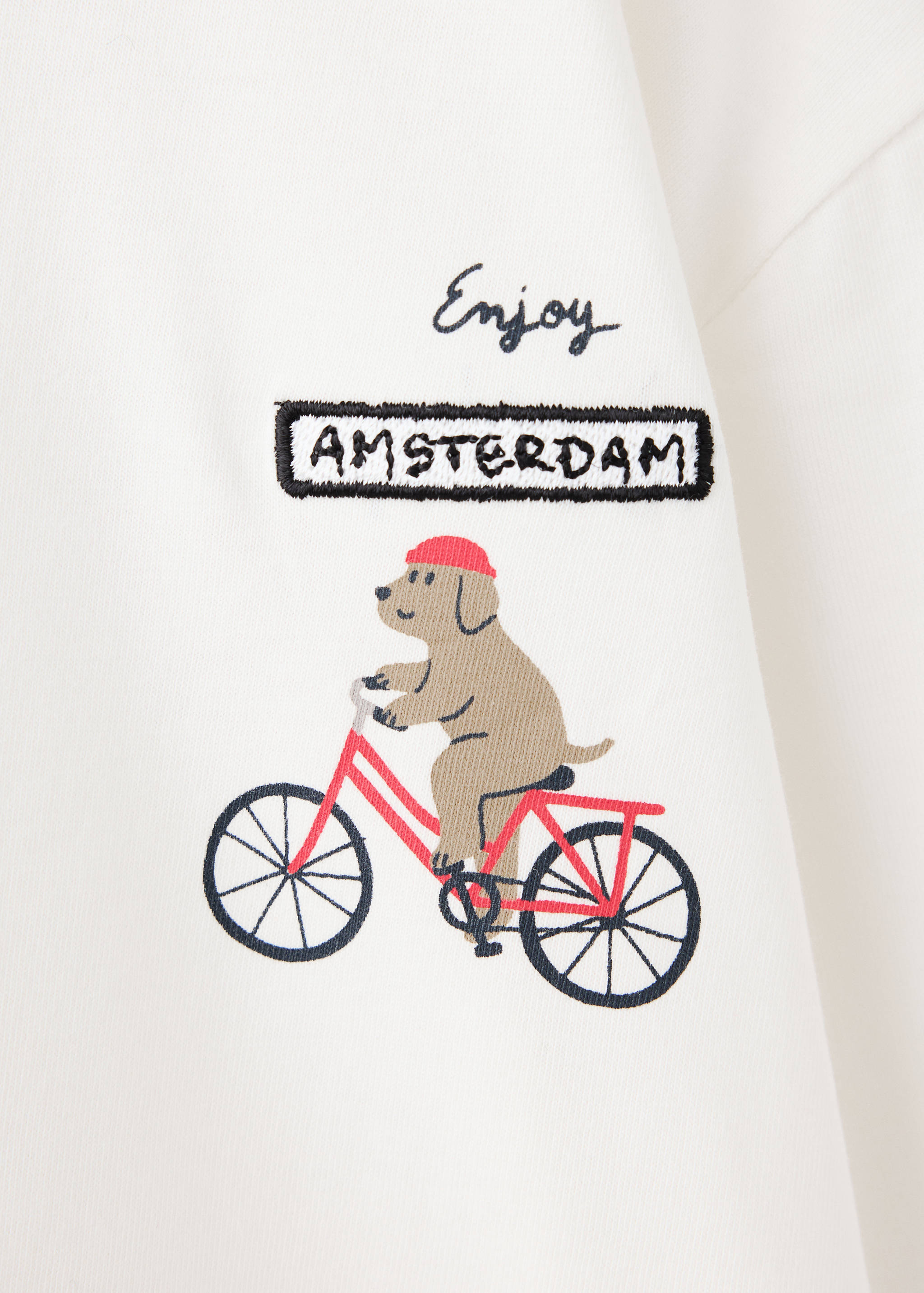 Close-up of a kids white t-shirt with an embroidered dog riding a bike.