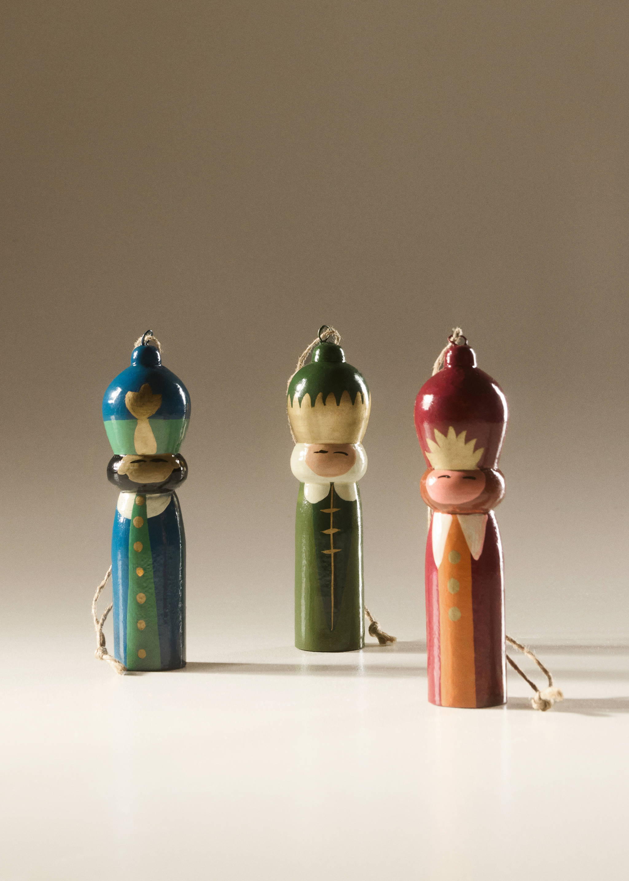 Three painted wooden Christmas ornaments shaped as stylized figures with twine loops.