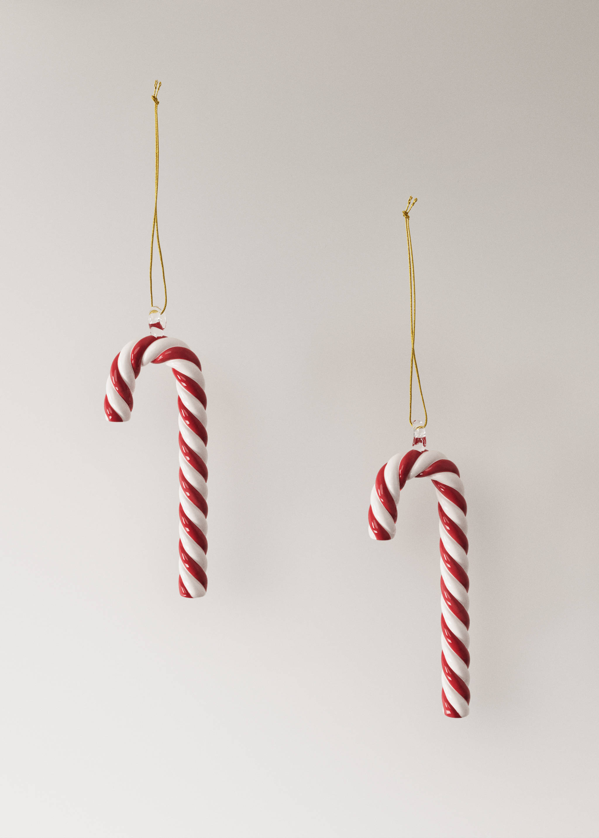 Two glossy red and white striped candy cane Christmas ornaments hanging on gold strings.