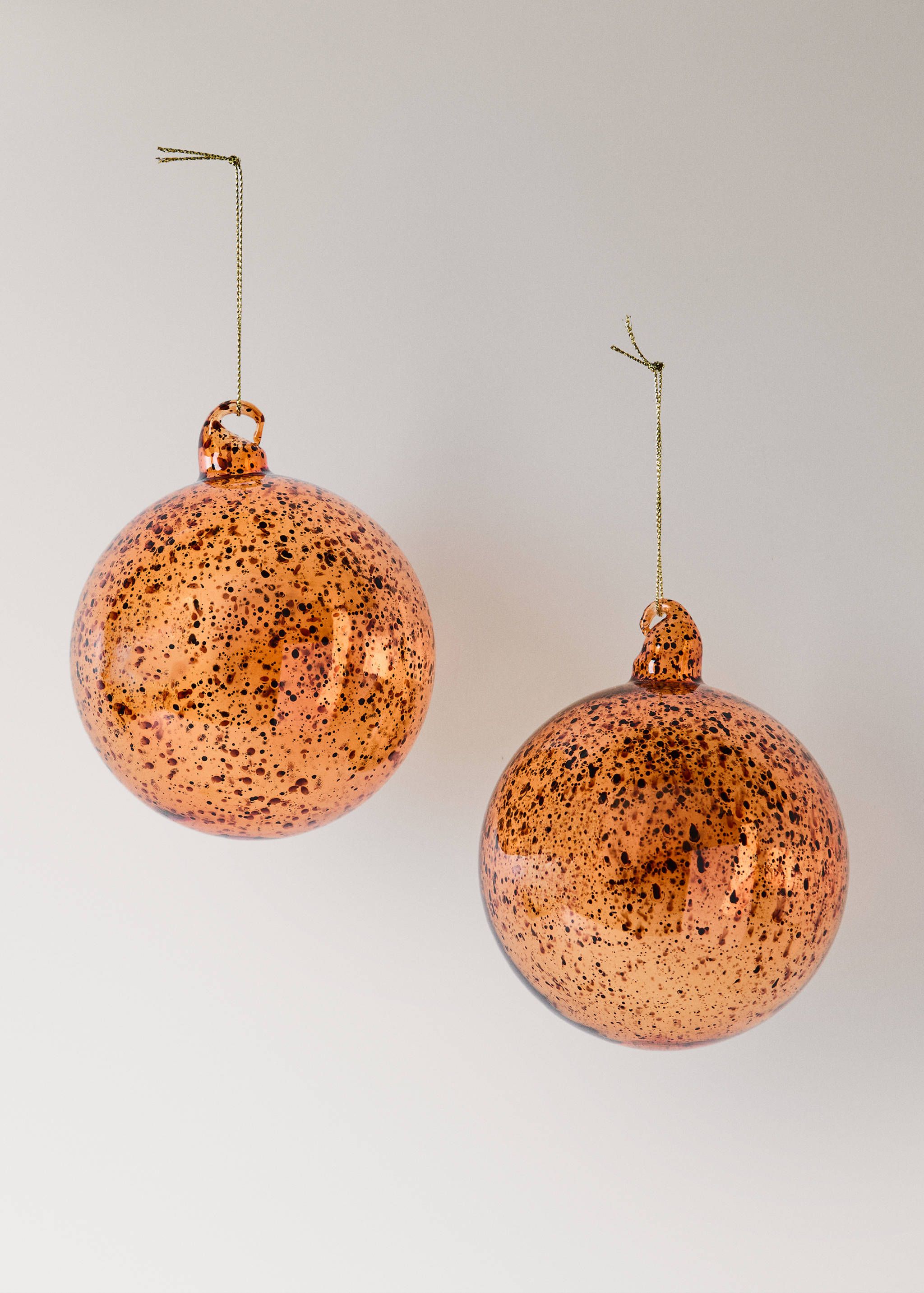Two speckled orange glass Christmas baubles hanging on gold threads.