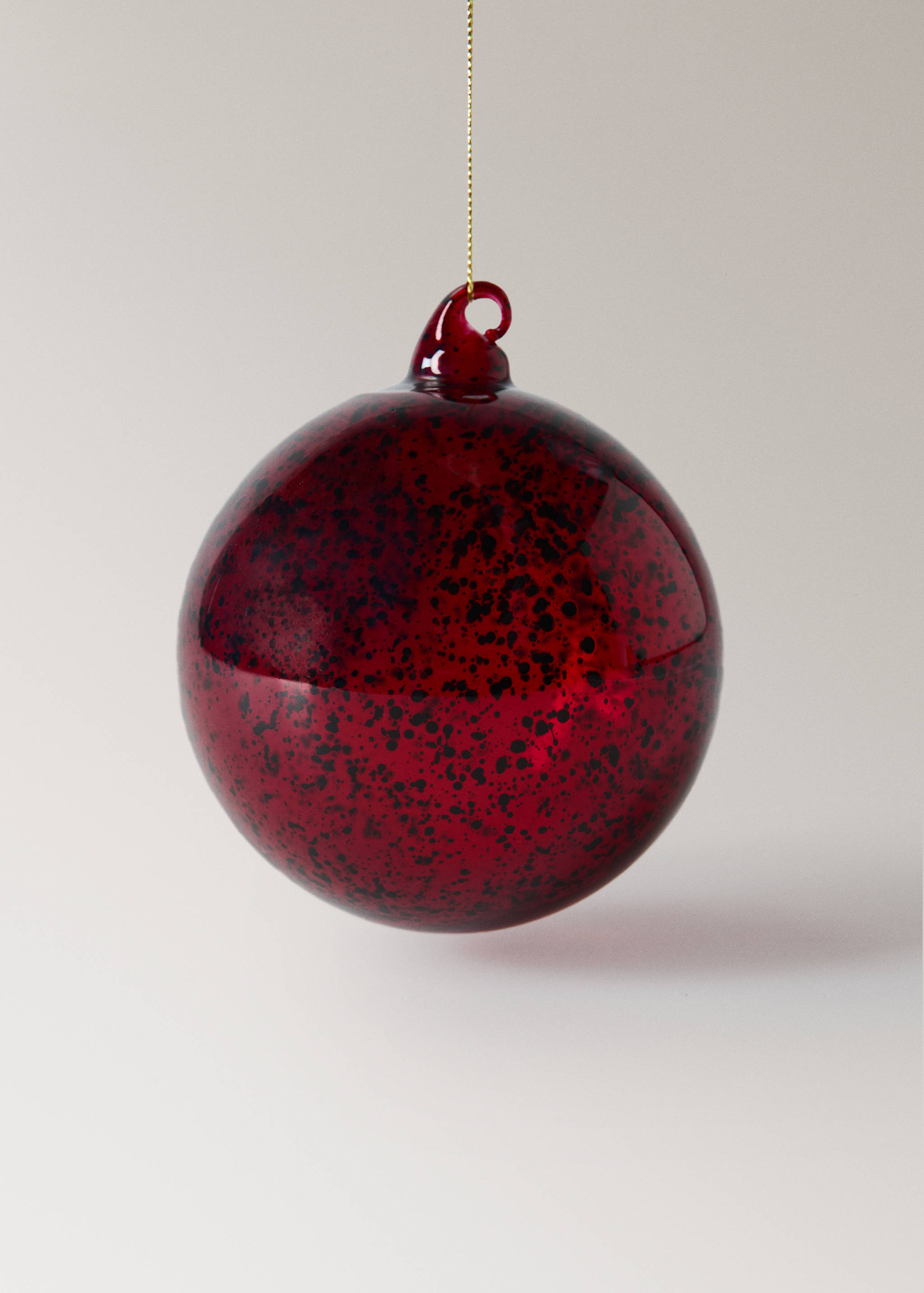 Red speckled glass Christmas decoration hanging from a gold string.