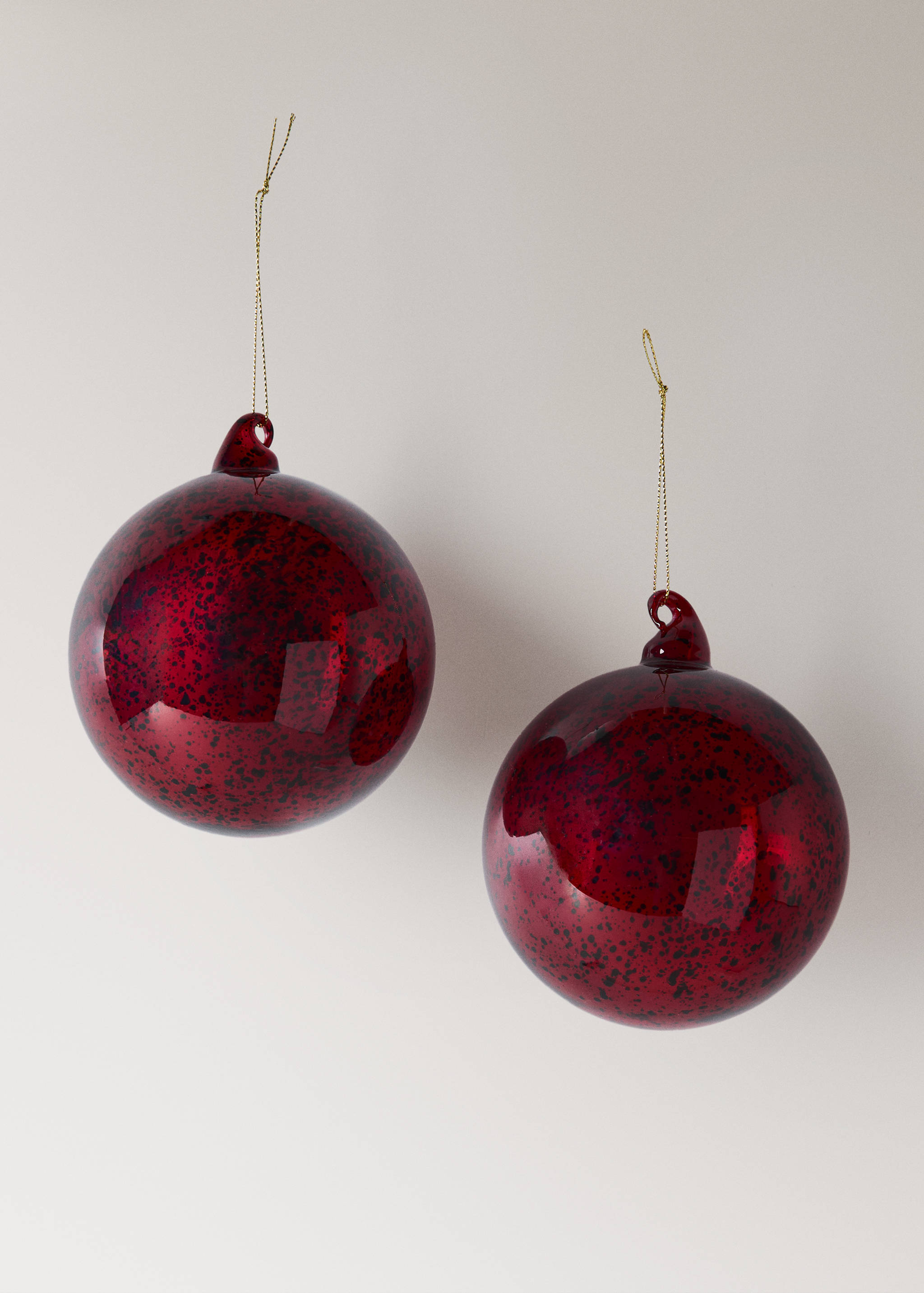 Two glossy red speckled glass Christmas ornaments hanging from gold cords.