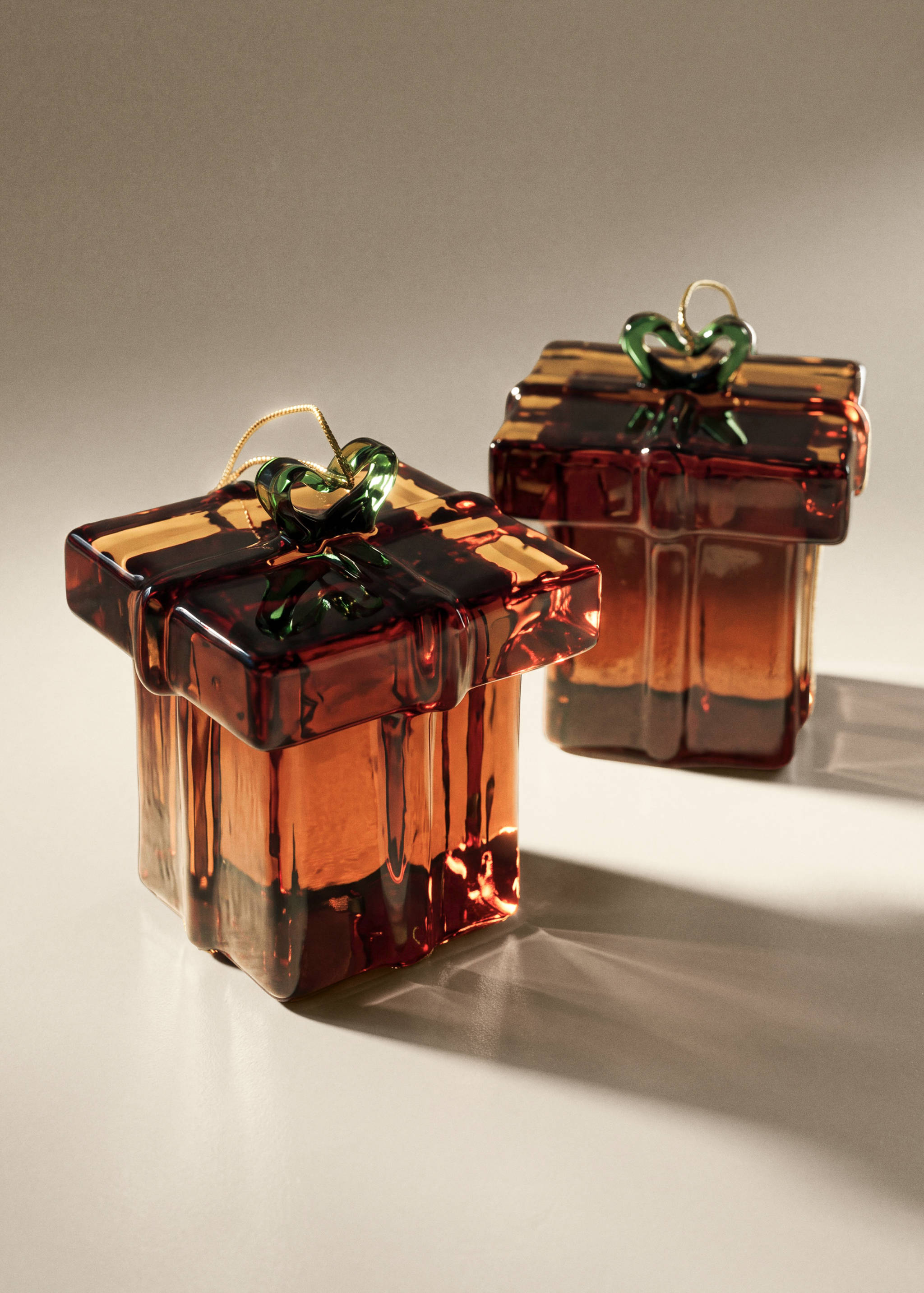 Two amber glass gift box Christmas ornaments with green bows.