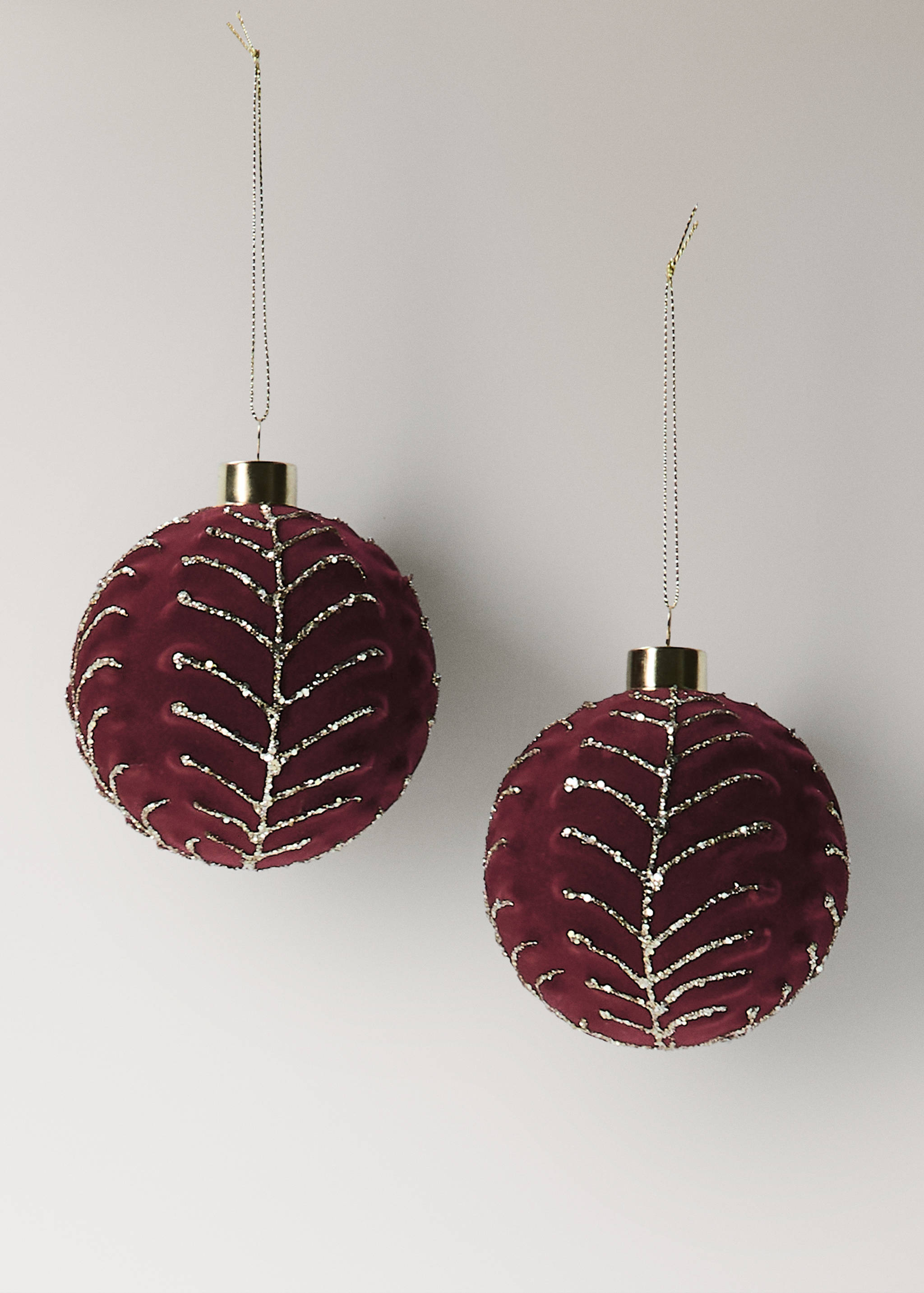 Two dark red velvet Christmas baubles with glittering gold leaf patterns and hanging strings.