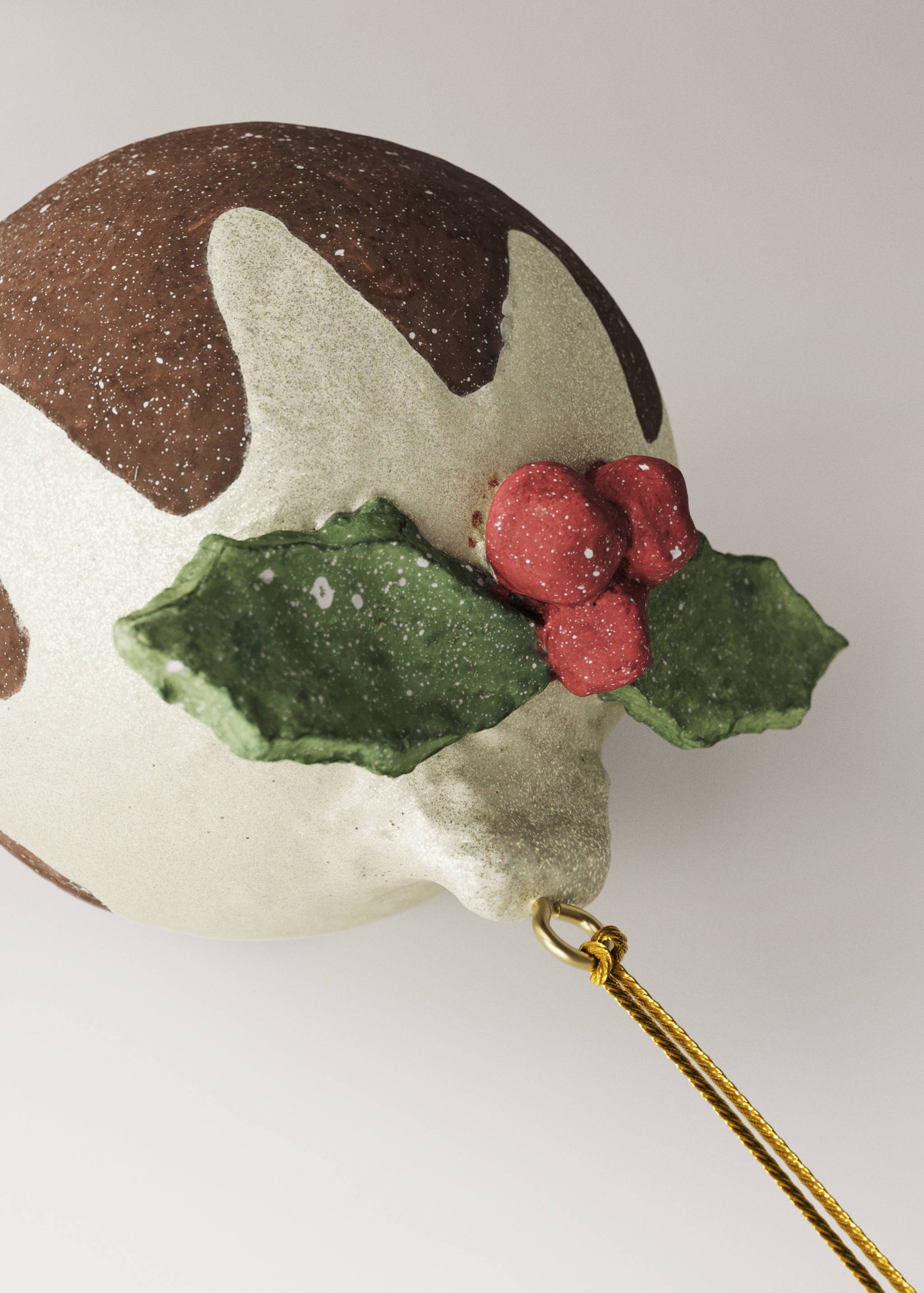 Christmas pudding hanging decoration with white icing, green leaves, and red berries.