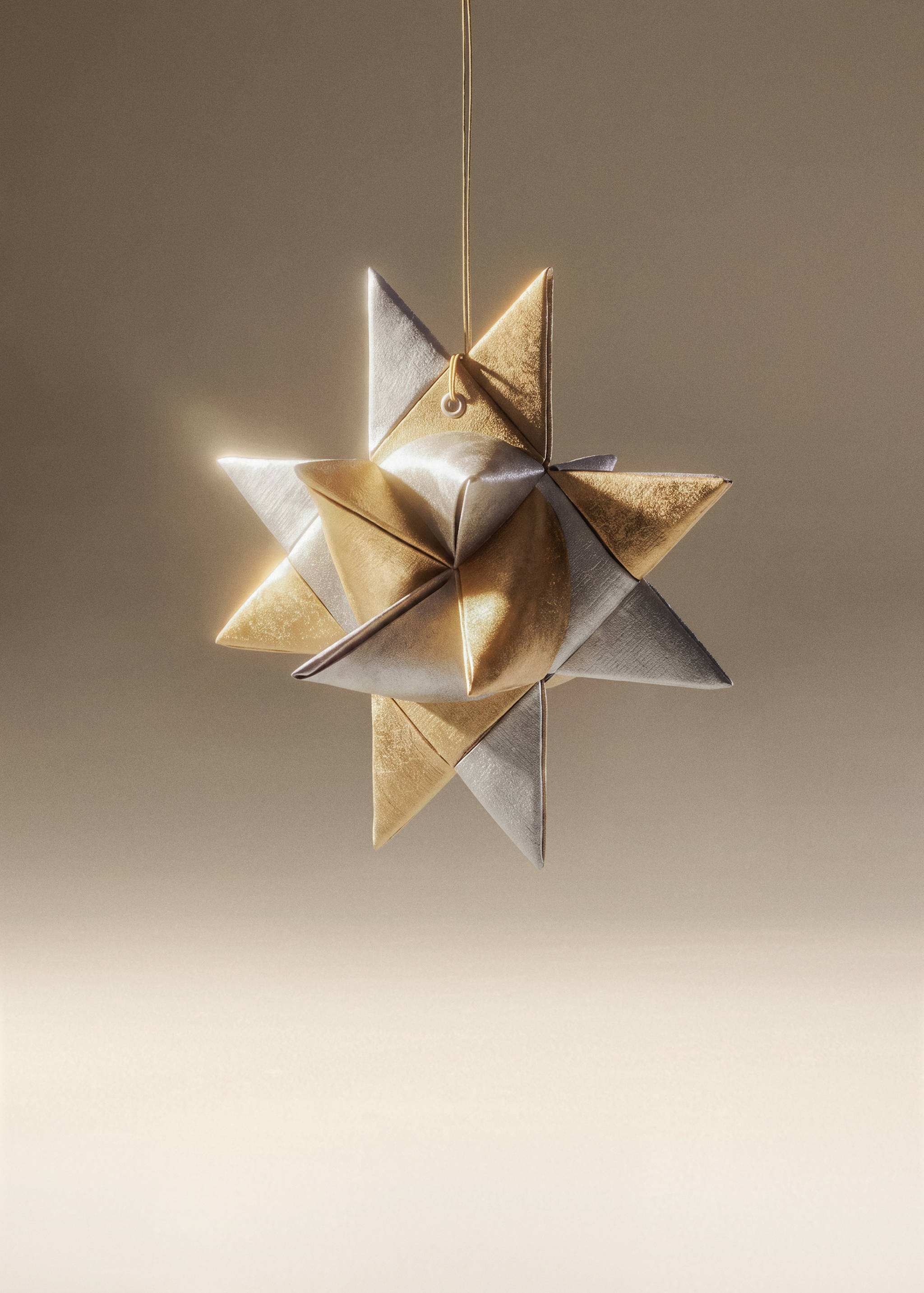 Metallic gold and silver folded star Christmas ornament hanging on a thin gold cord.