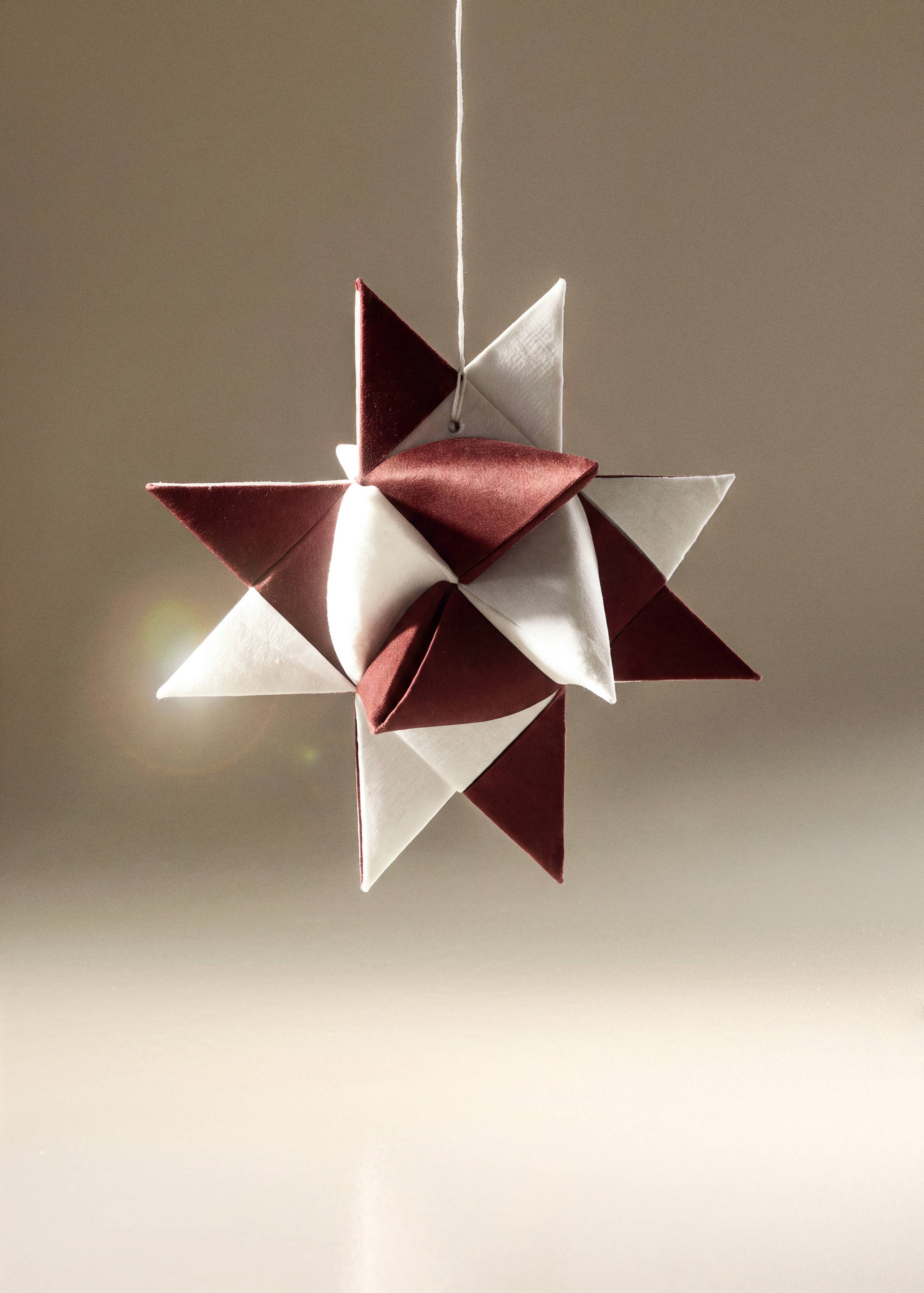 Hanging Christmas star decoration in dark red and white fabric.