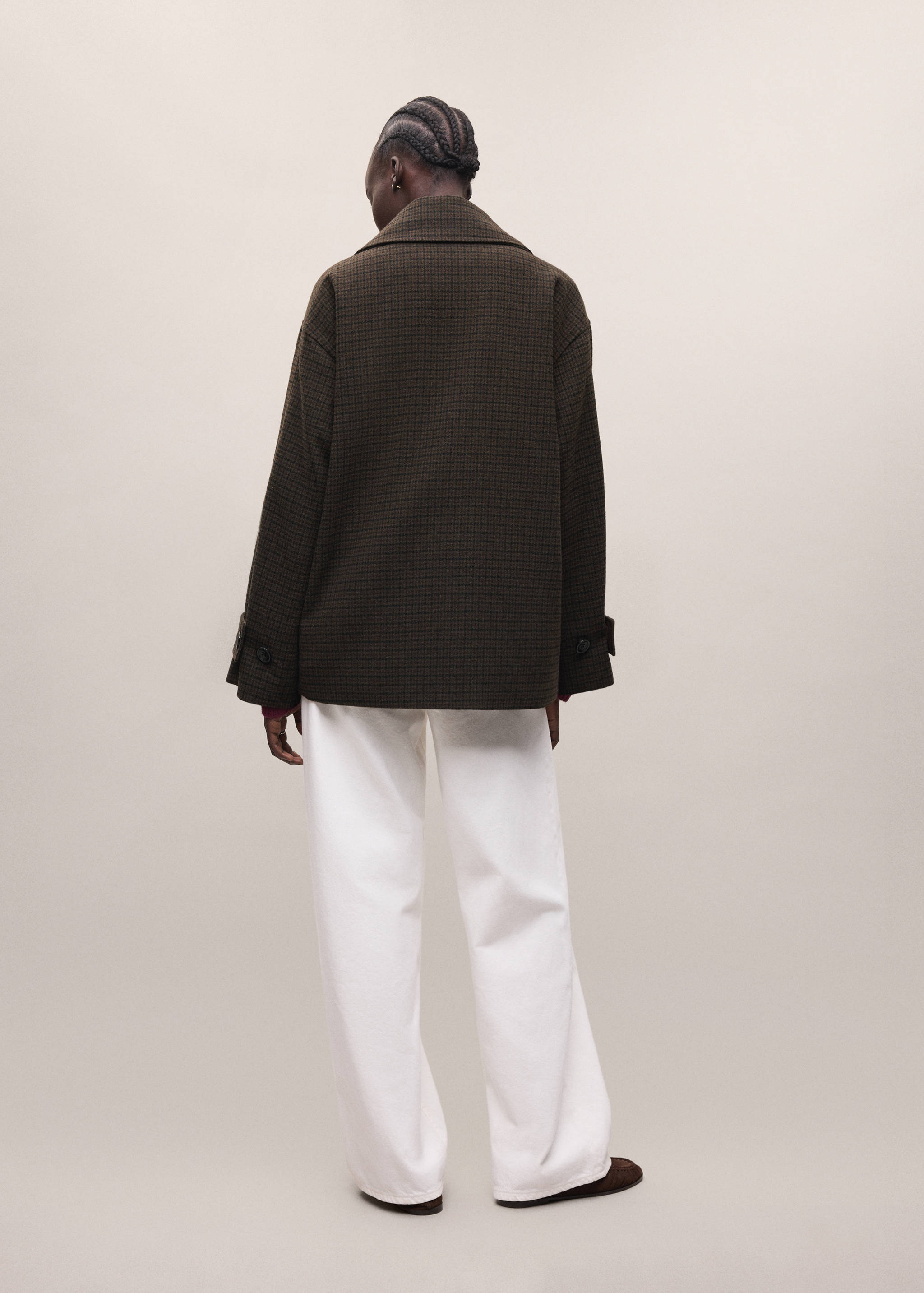 Back view of a dark green checked coat with a lapel collar and wide-leg white trousers.