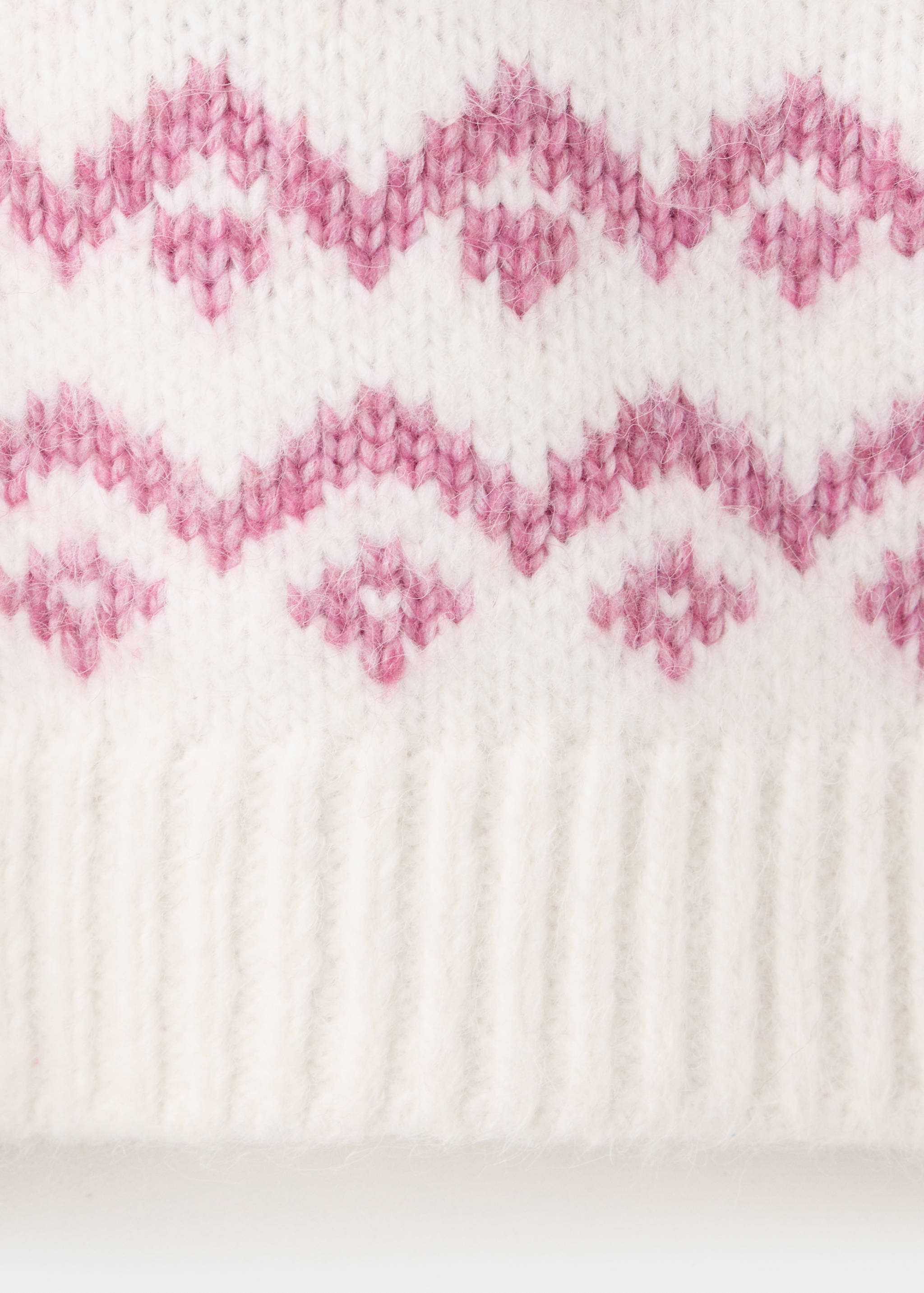 Close-up of a fuzzy white knitted jersey with a pink fair isle pattern and ribbed hem.