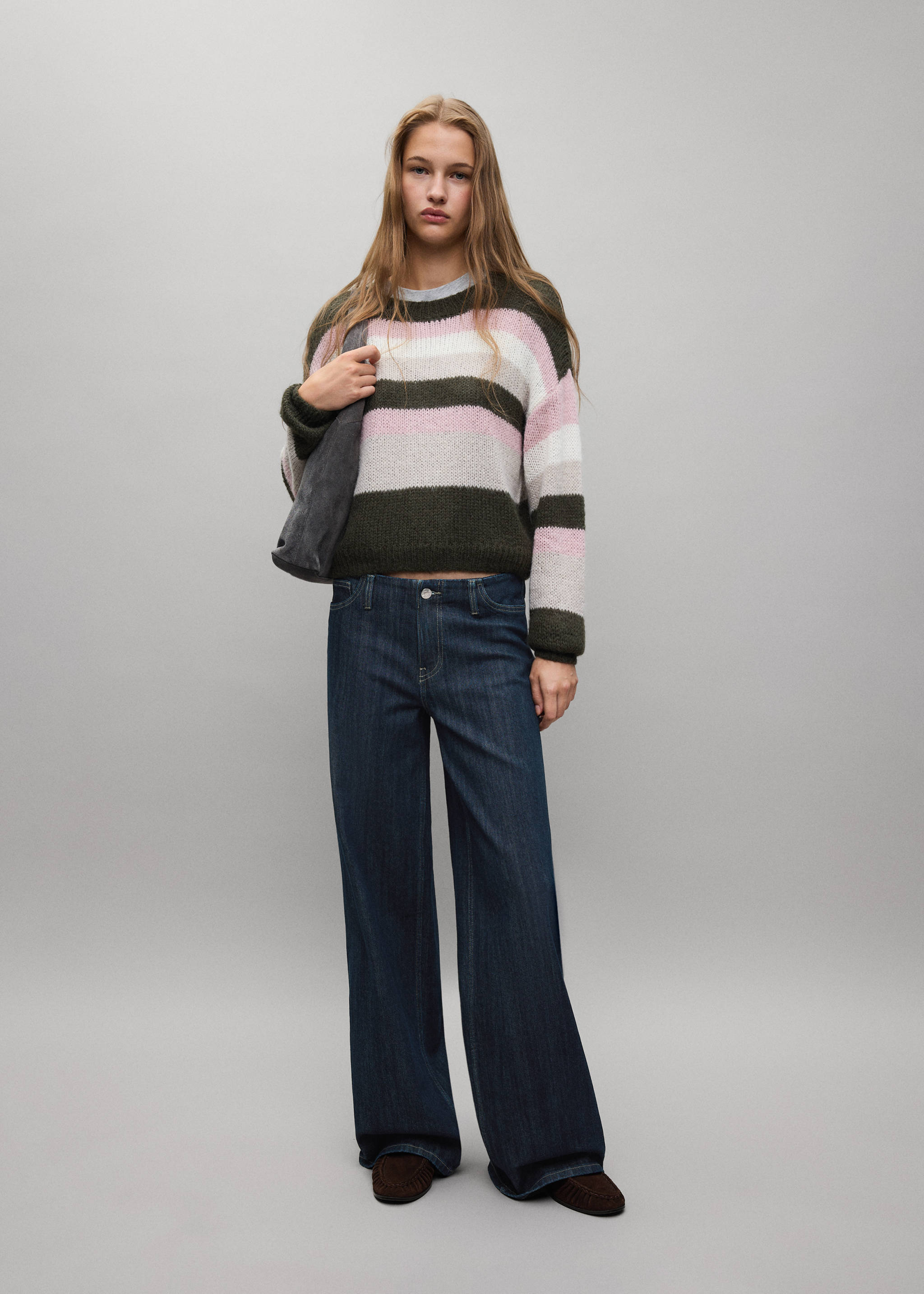 Striped knit jersey in dark green, pink, and white, worn with dark denim trousers.
