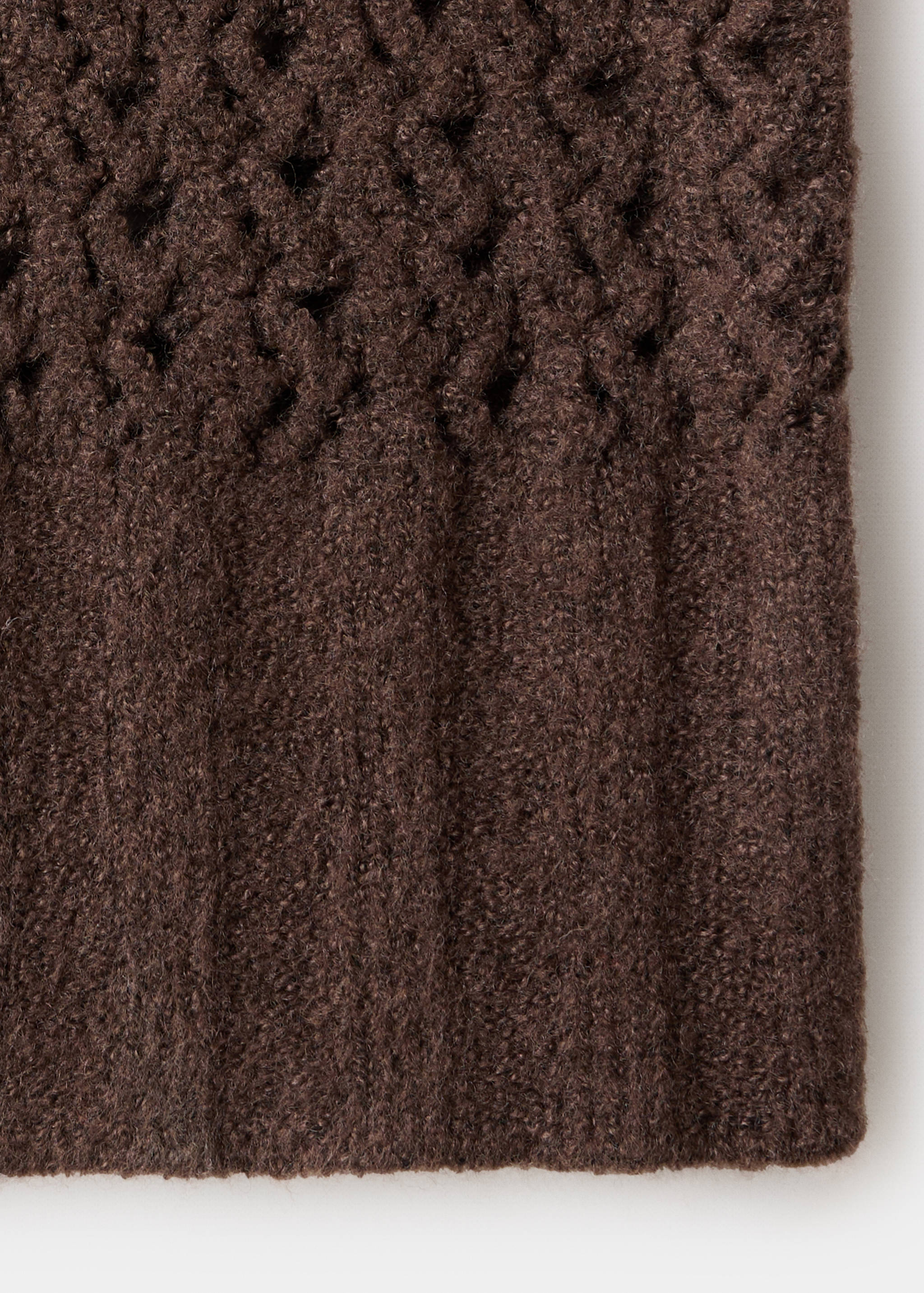 Brown jersey fabric close-up showing openwork knit and ribbed hem.