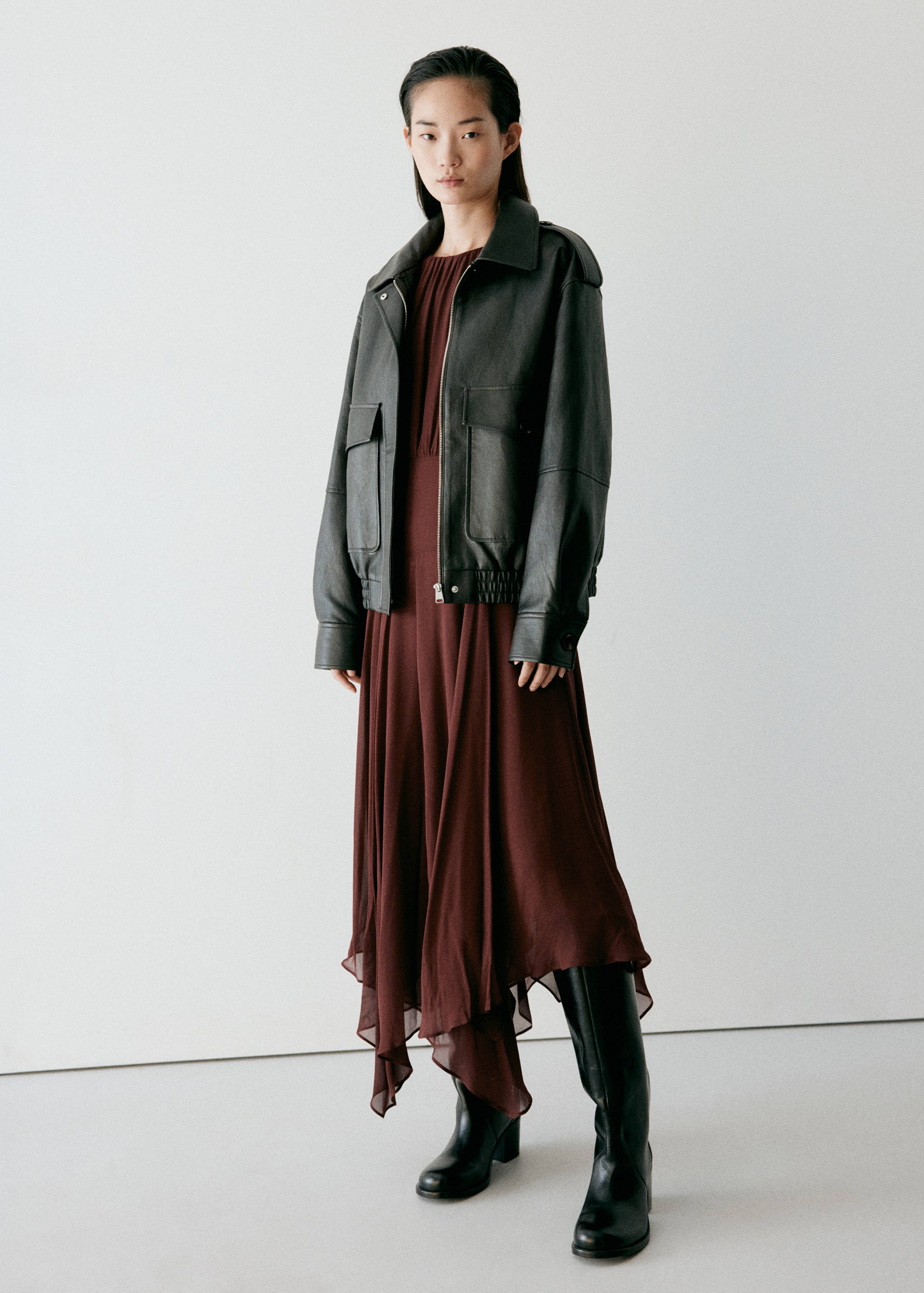 Burgundy midi dress with gathered neckline and asymmetrical hem, styled with a leather jacket.