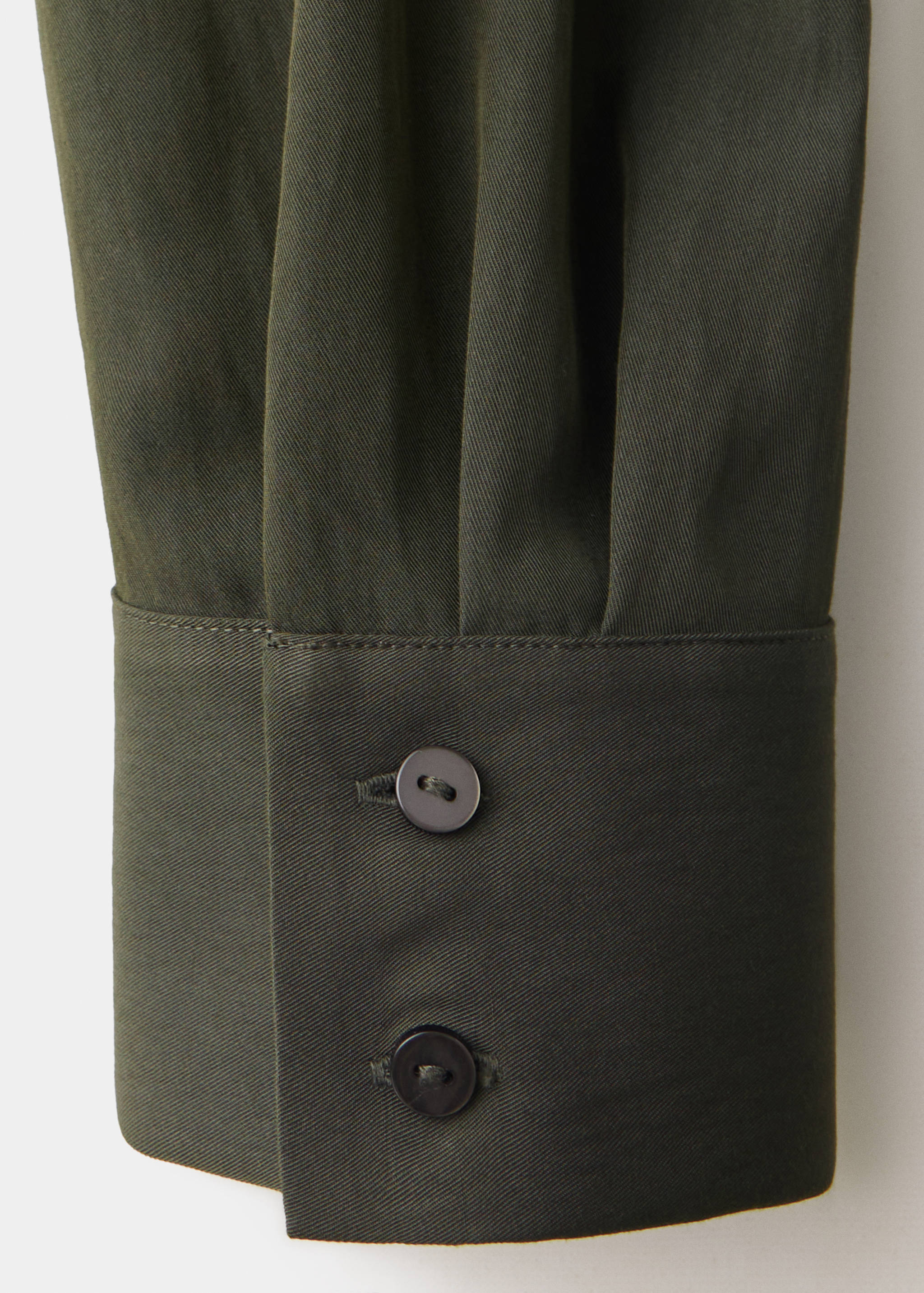 Close-up of olive green dress cuff with two dark buttons and pleats.