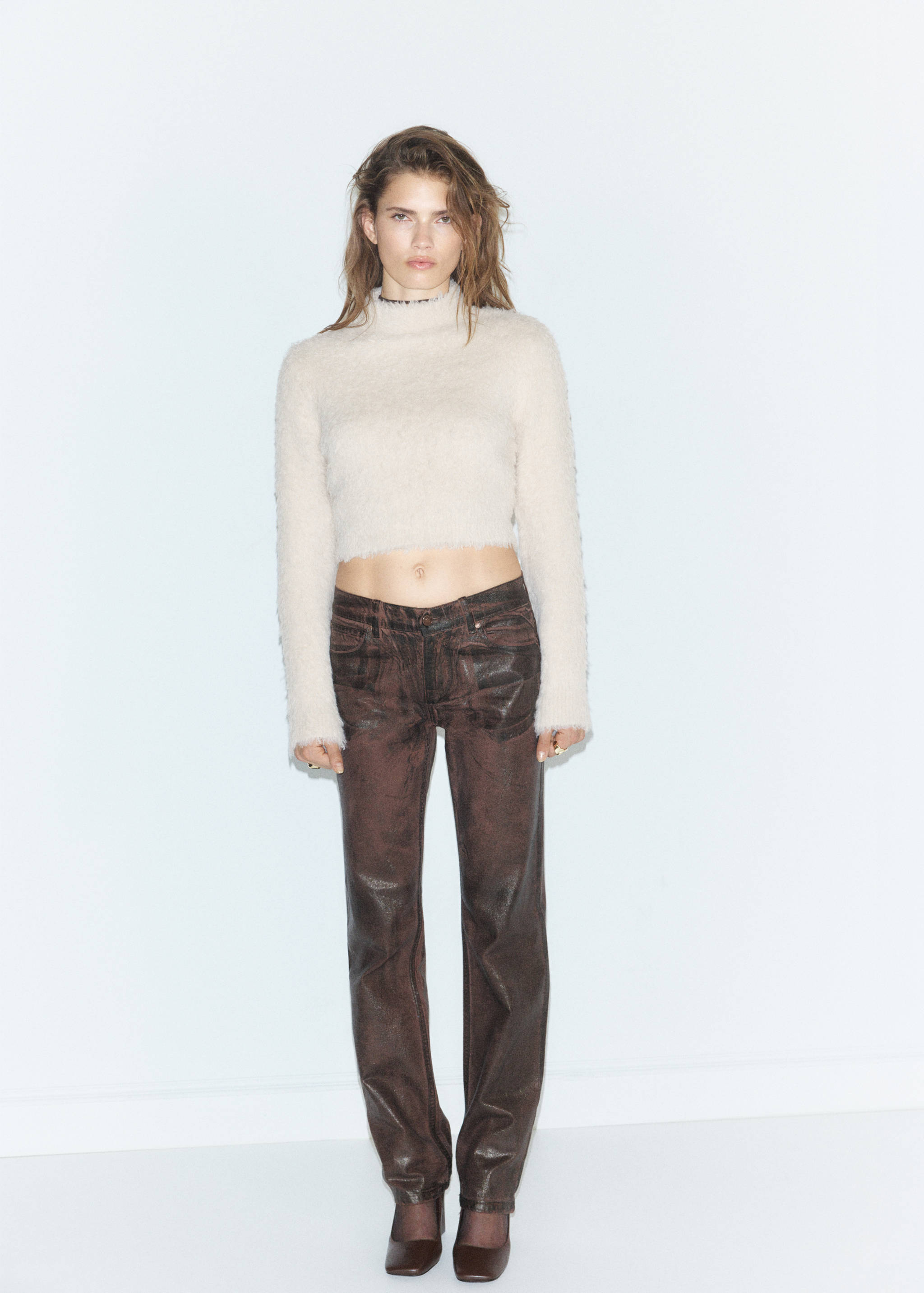 Pale pink high-neck knit jersey sweater with long sleeves, worn with dark trousers.