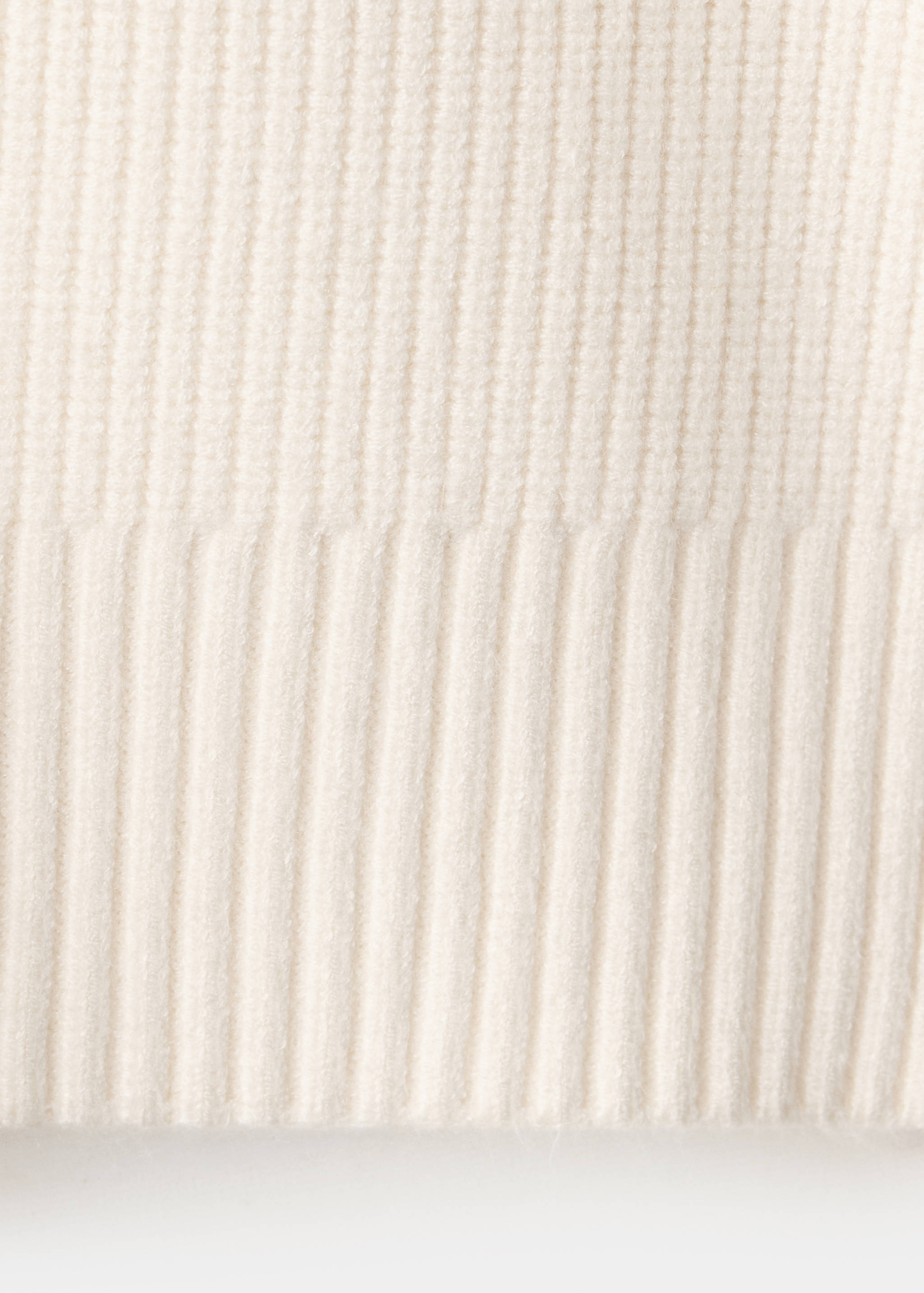 Detalle del tejido de punto canalé texturizado de un jersey beige claro.