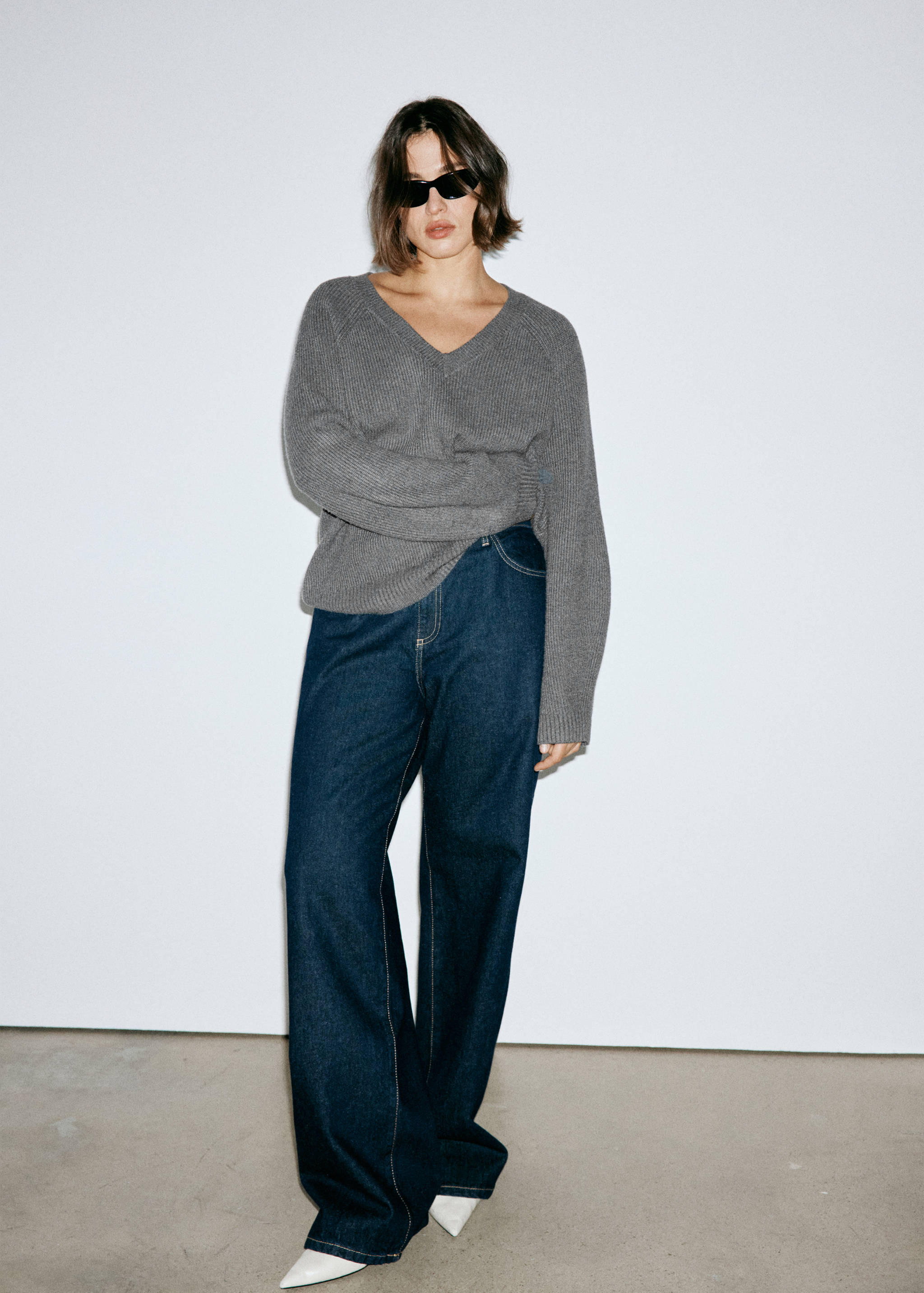 Jersey de punto gris con cuello en V y manga larga, combinado con pantalones vaqueros de denim azul oscuro.