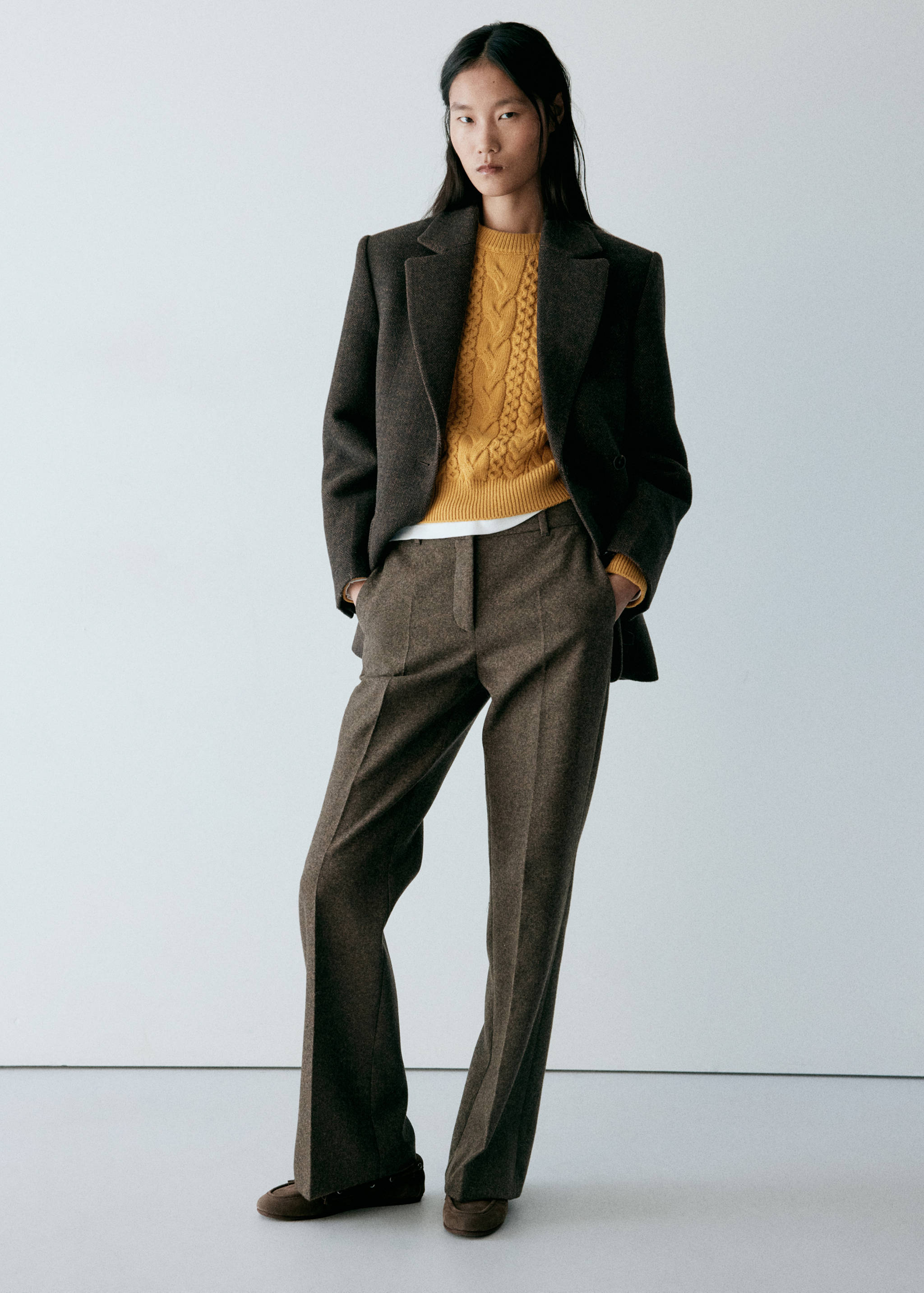 Yellow cable-knit jersey worn under a brown blazer with matching trousers.