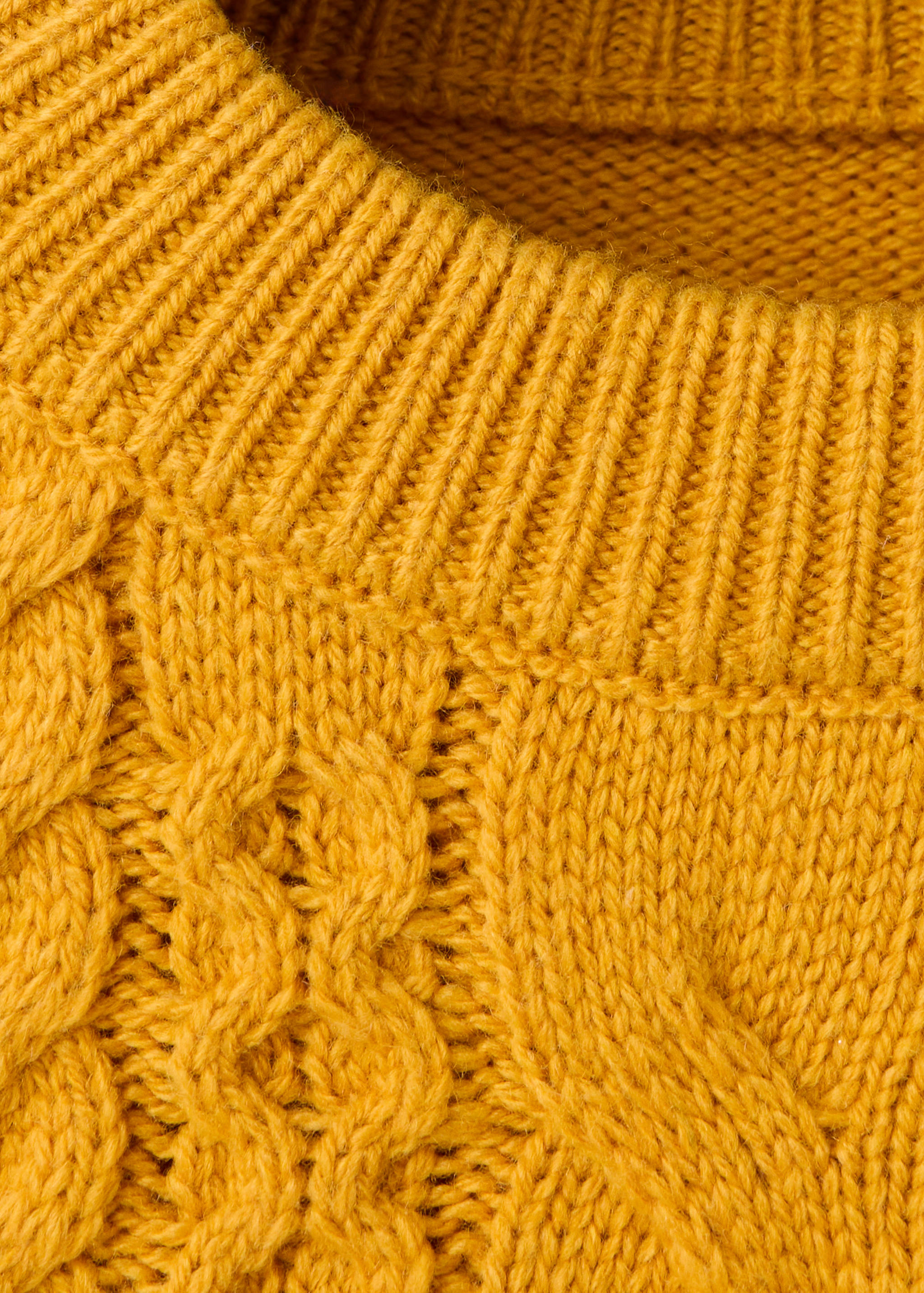 Close-up of a yellow cable-knit jumper with a ribbed neckline.