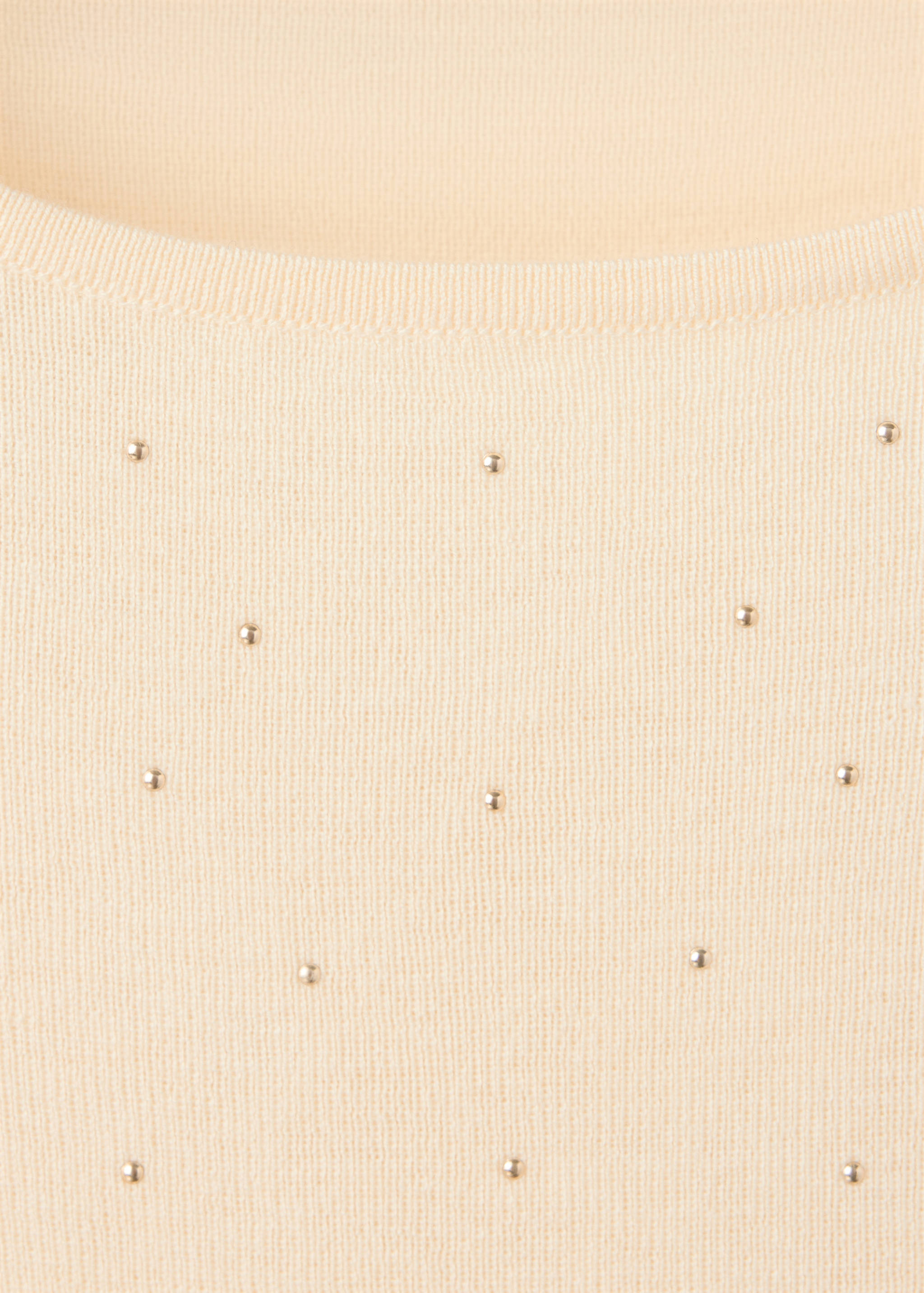 Detalle del cuello de jersey de punto crema con aplicaciones de tachuelas metálicas.