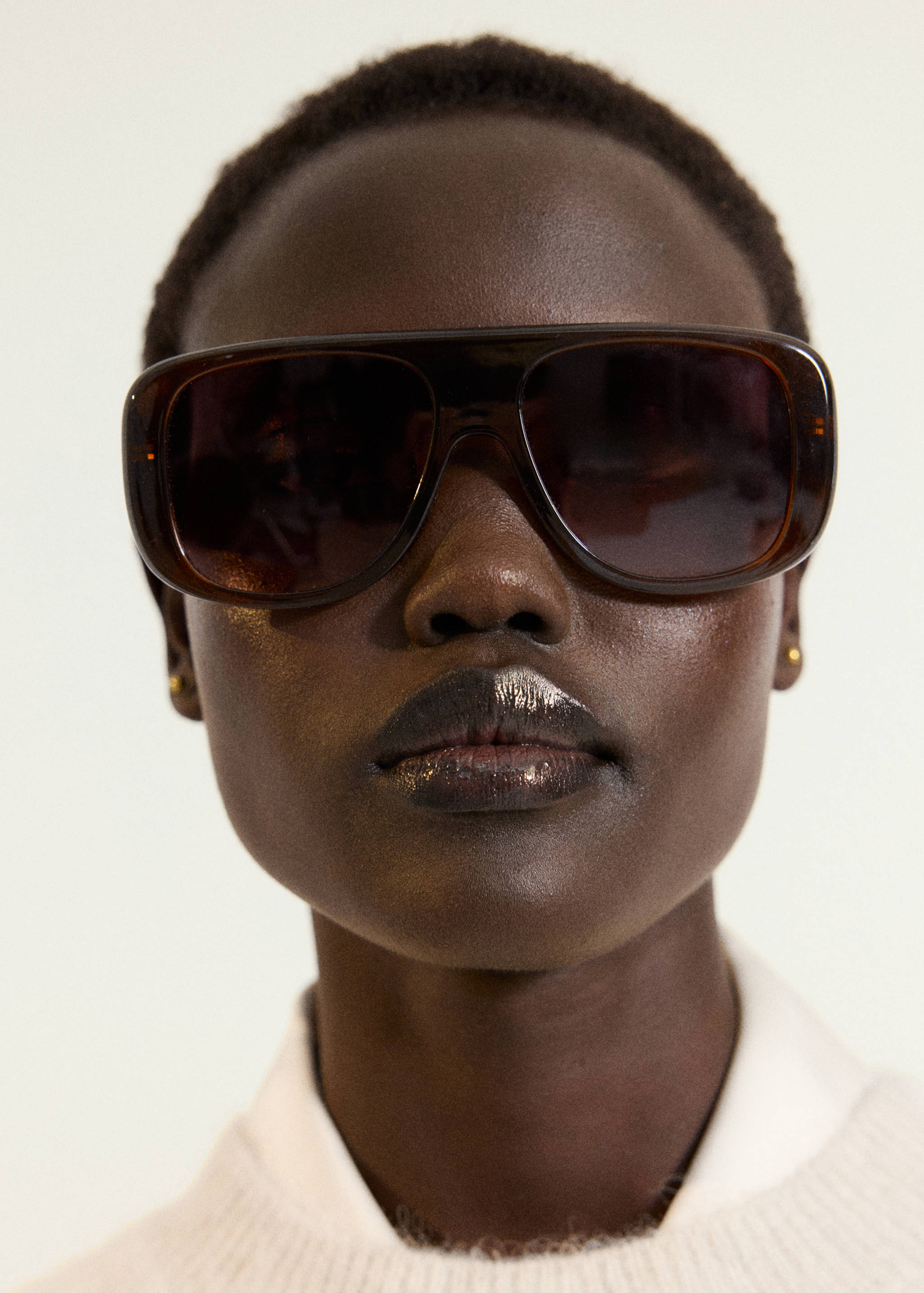 Close-up of a model wearing dark brown sunglasses and a ribbed knit jersey.