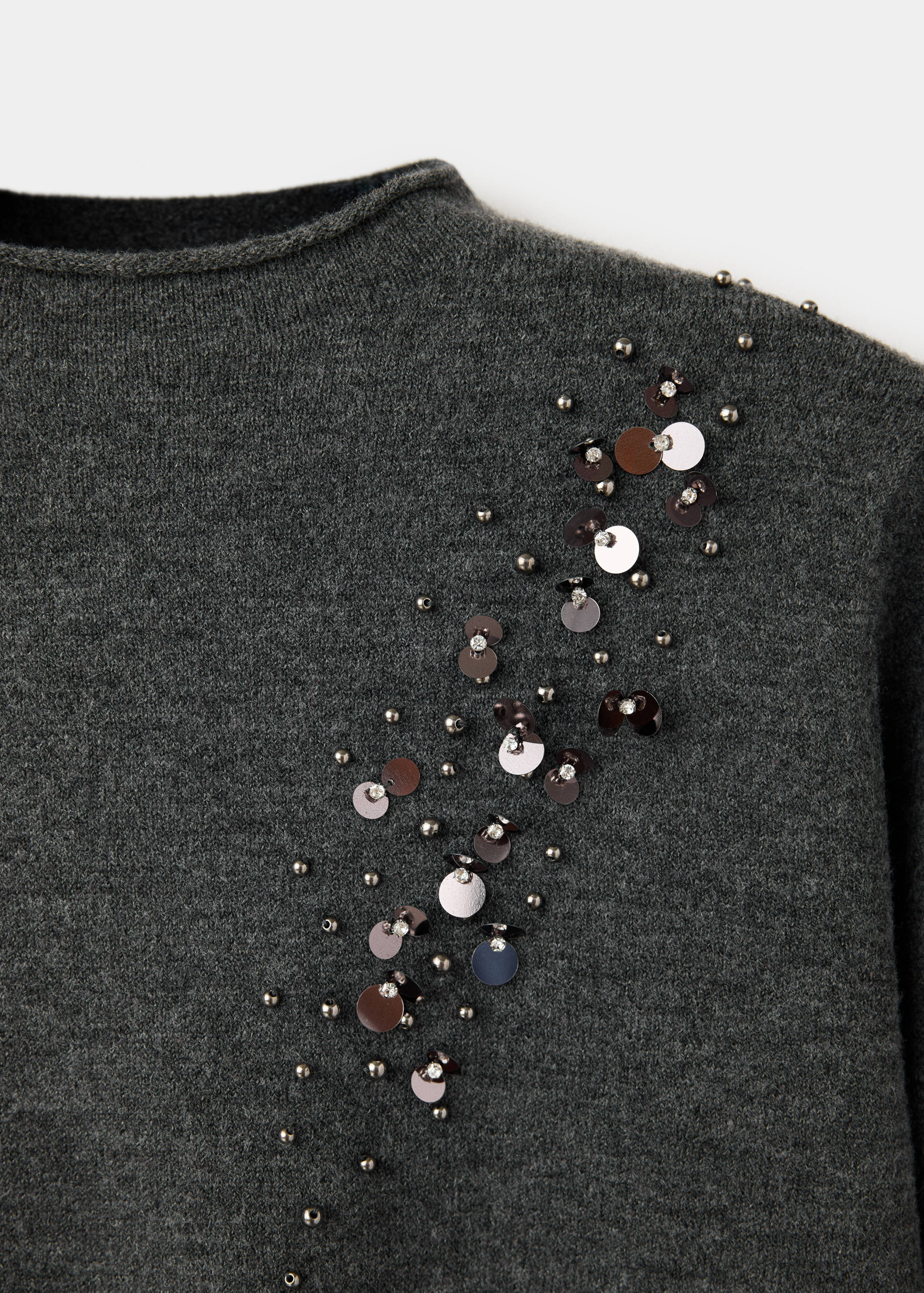 Dark grey knit jersey close-up featuring a diagonal cluster of metallic beads, sequins, and rhinestones.