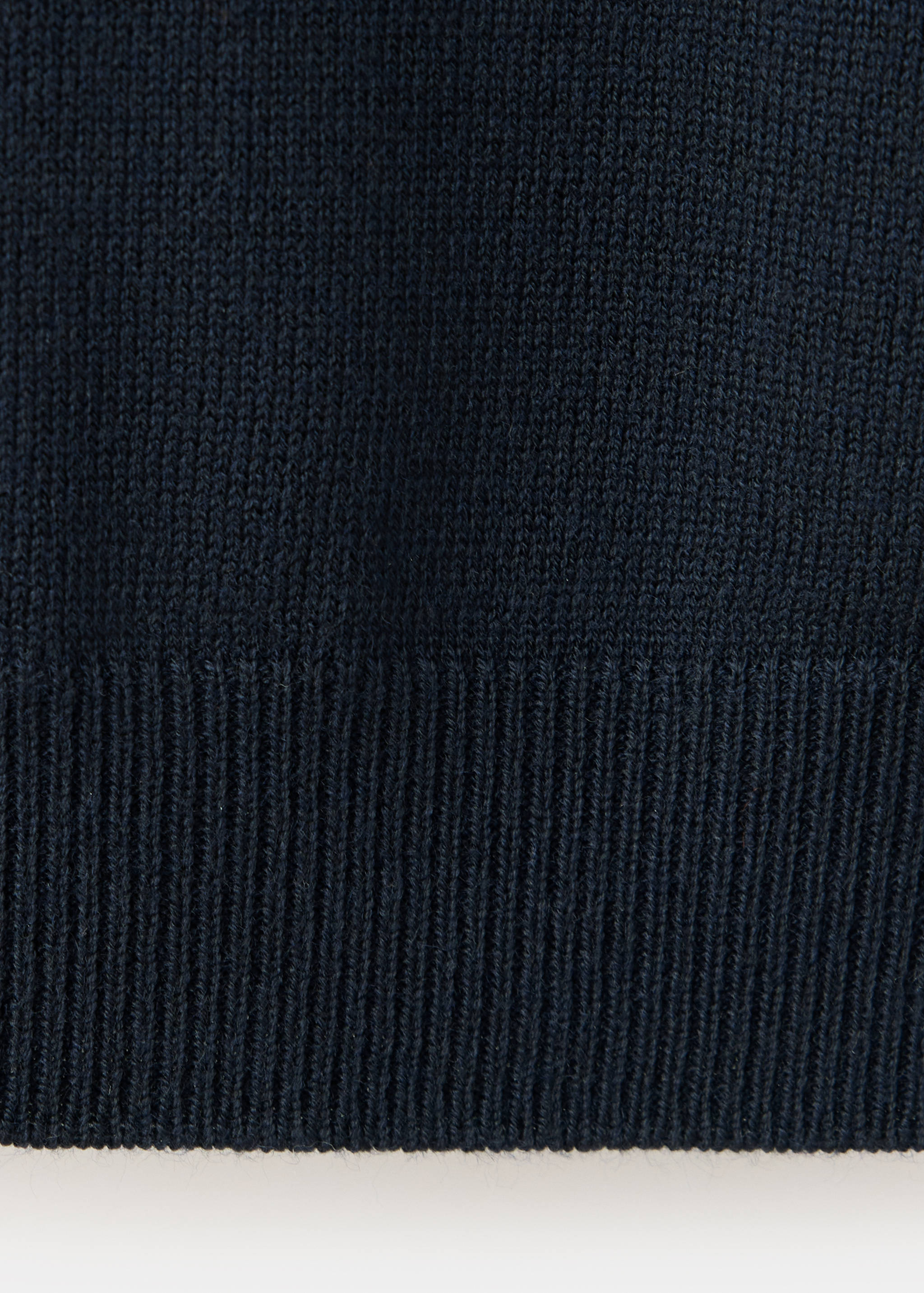 Close-up of a dark blue sweater knit fabric showing the ribbed hem.