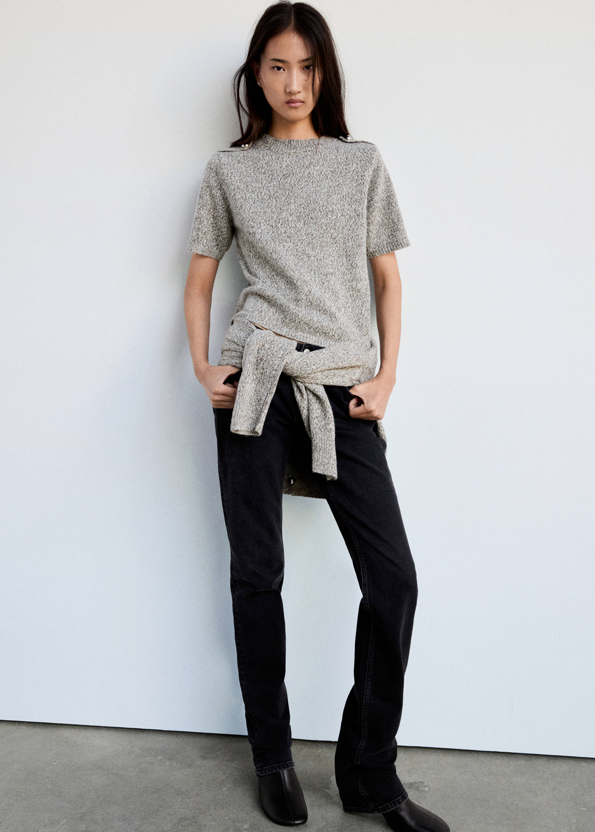 Grey mottled short-sleeved knit jumper with shoulder buttons, worn with dark trousers.