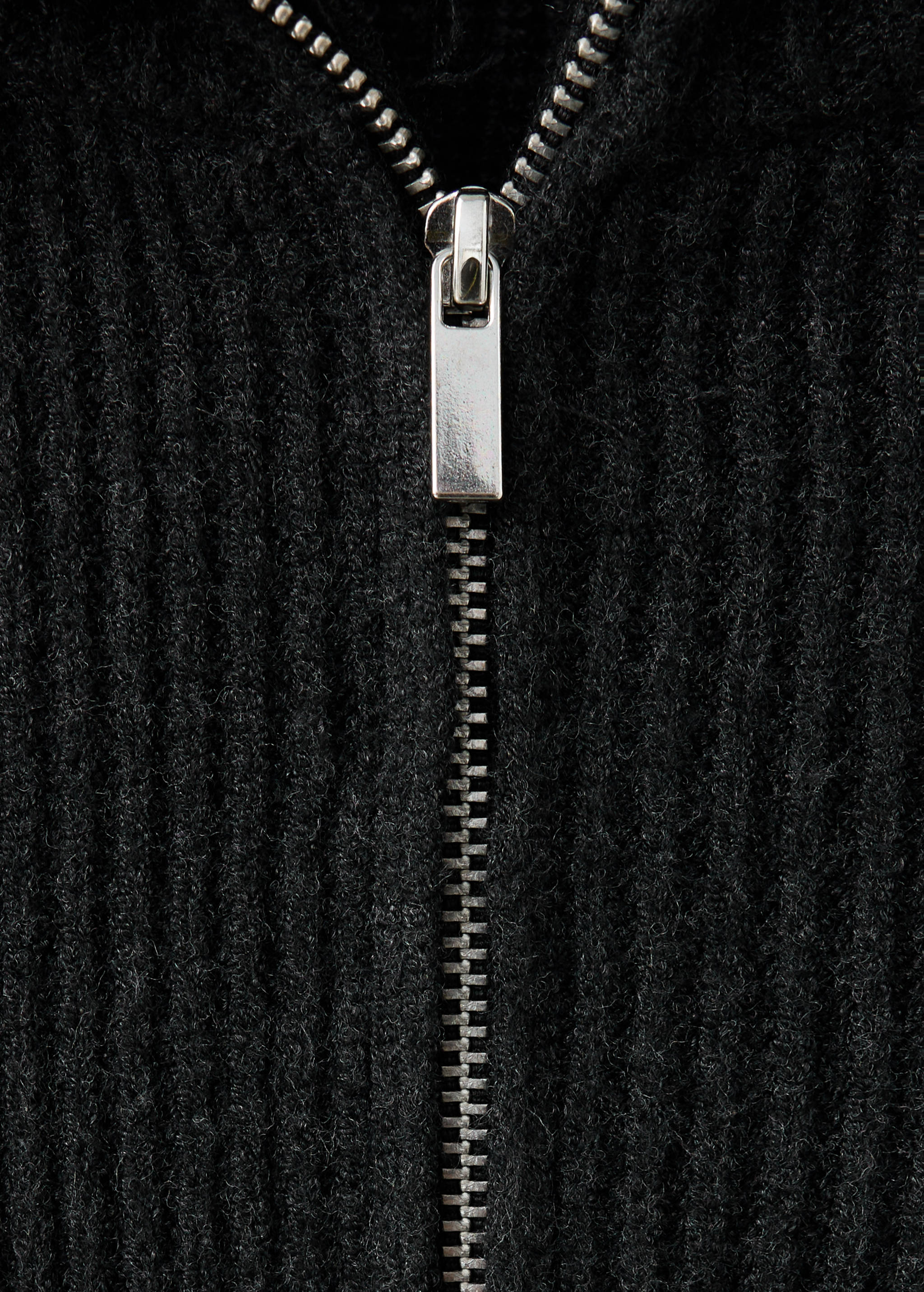 Close-up of a black ribbed jersey with a silver-toned metal zipper.