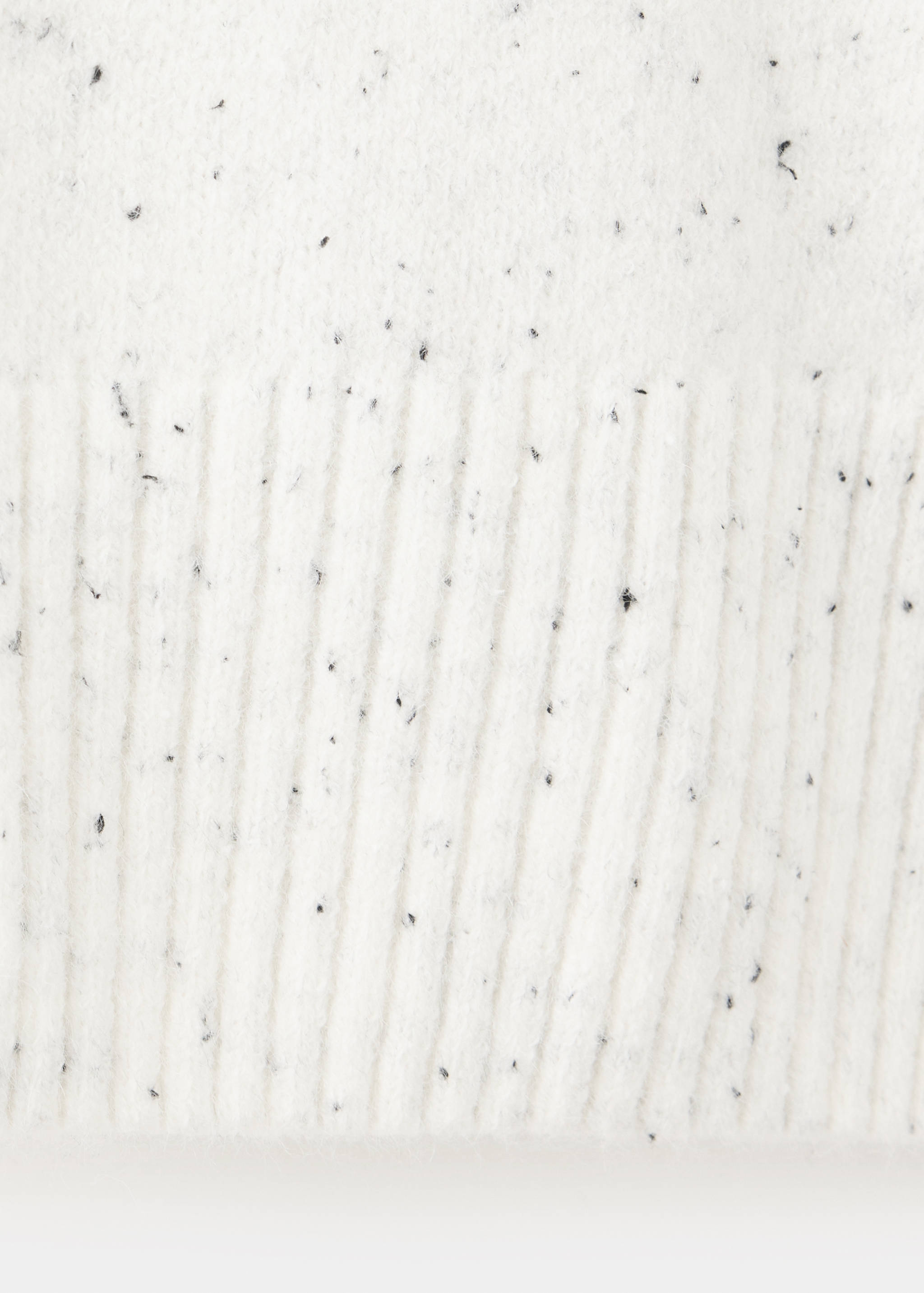Close-up of a white speckled jumper fabric texture with a ribbed hem.