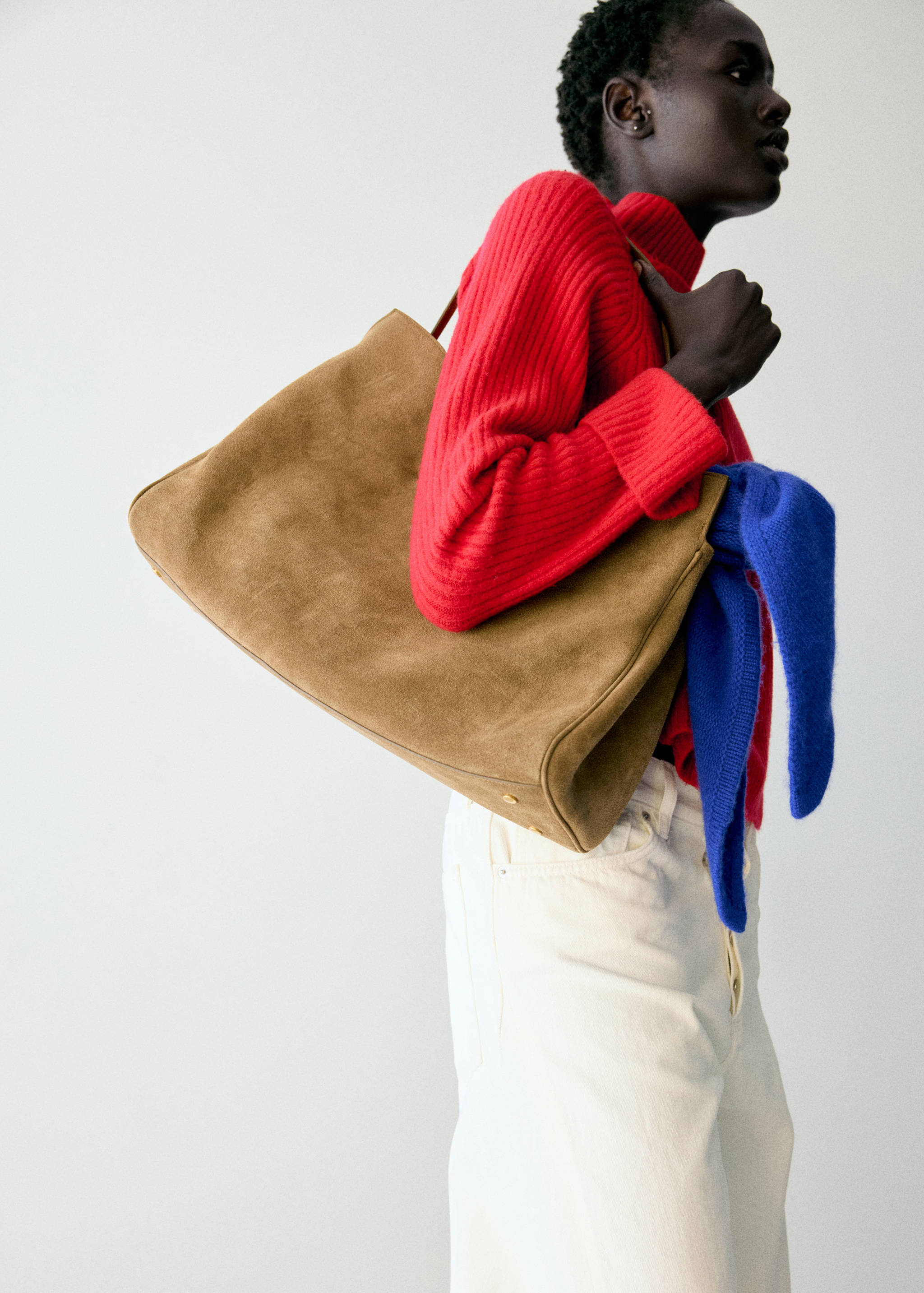 Red ribbed knit jersey with high neckline, worn with white trousers and a brown suede tote bag.