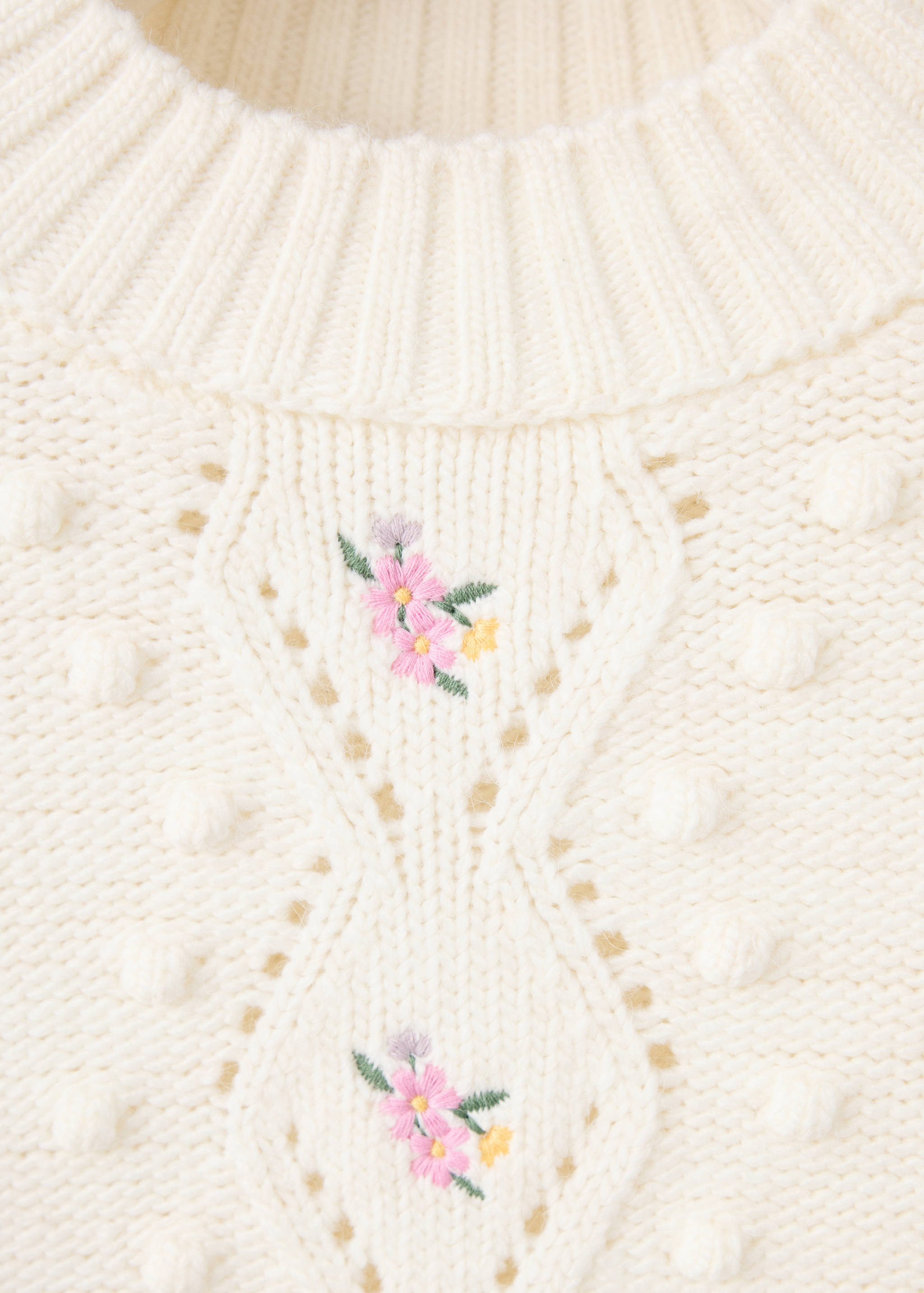 Close-up of an off-white knit jumper with floral embroidery and bobbles.
