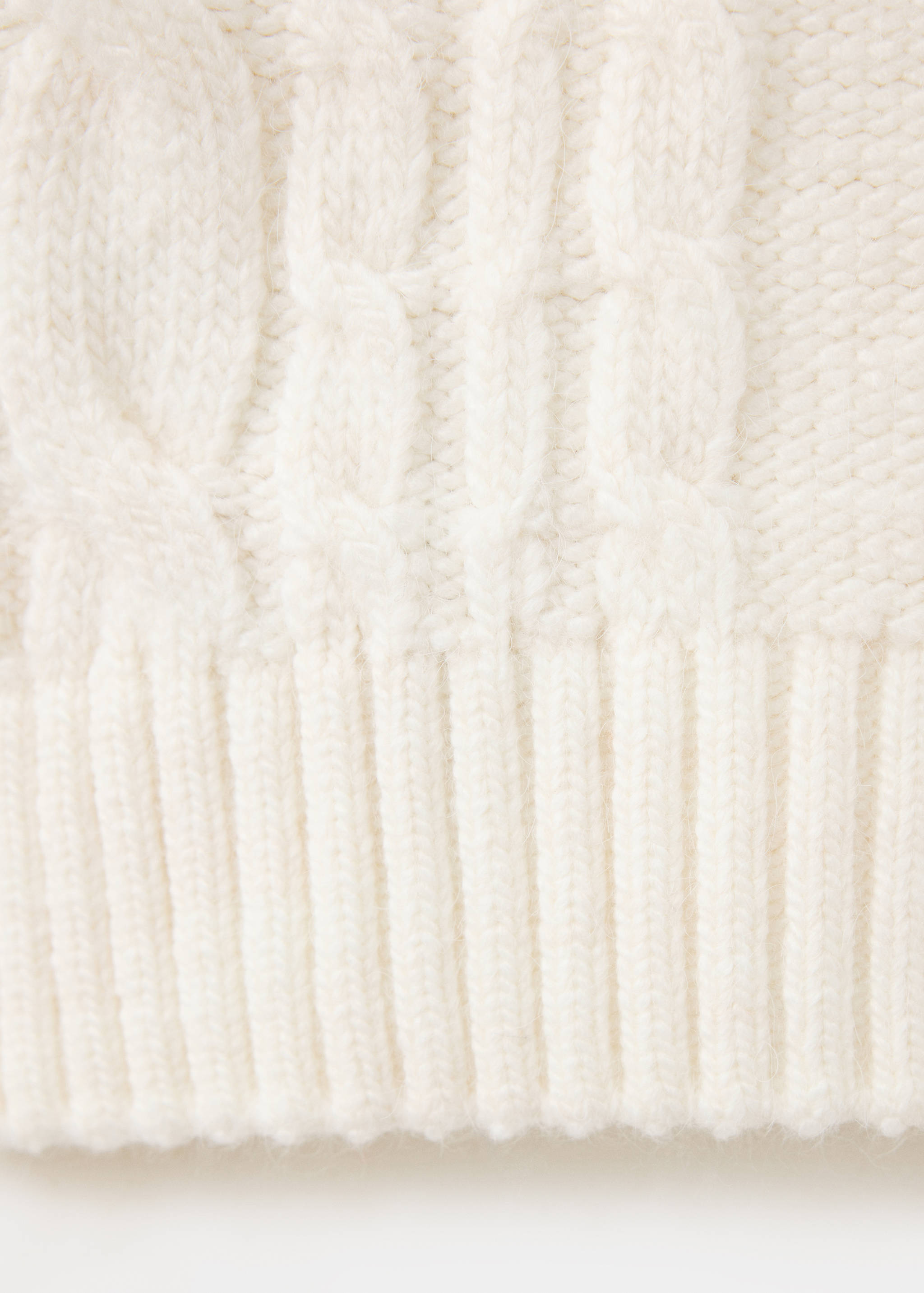 Close-up of a white cable-knit jumper showing the textured knit and ribbed hem.