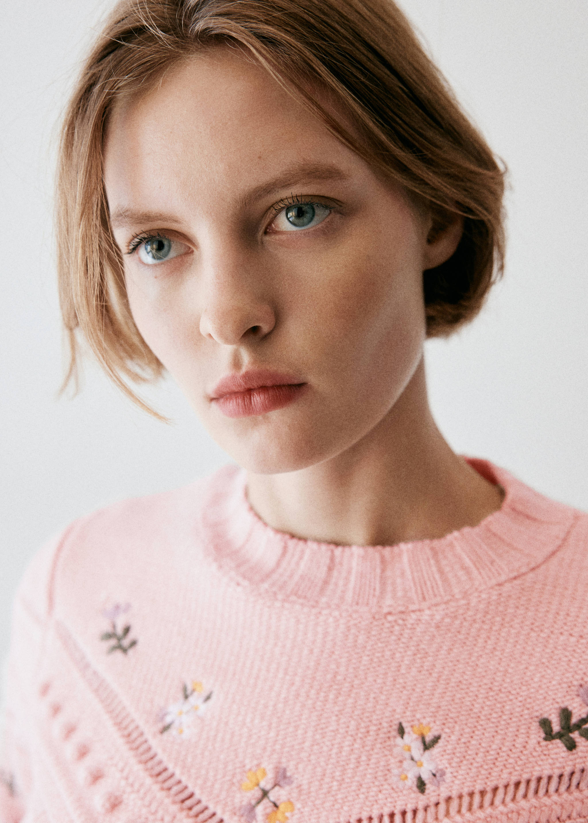 Close-up of a pink knit sweater with floral embroidery.