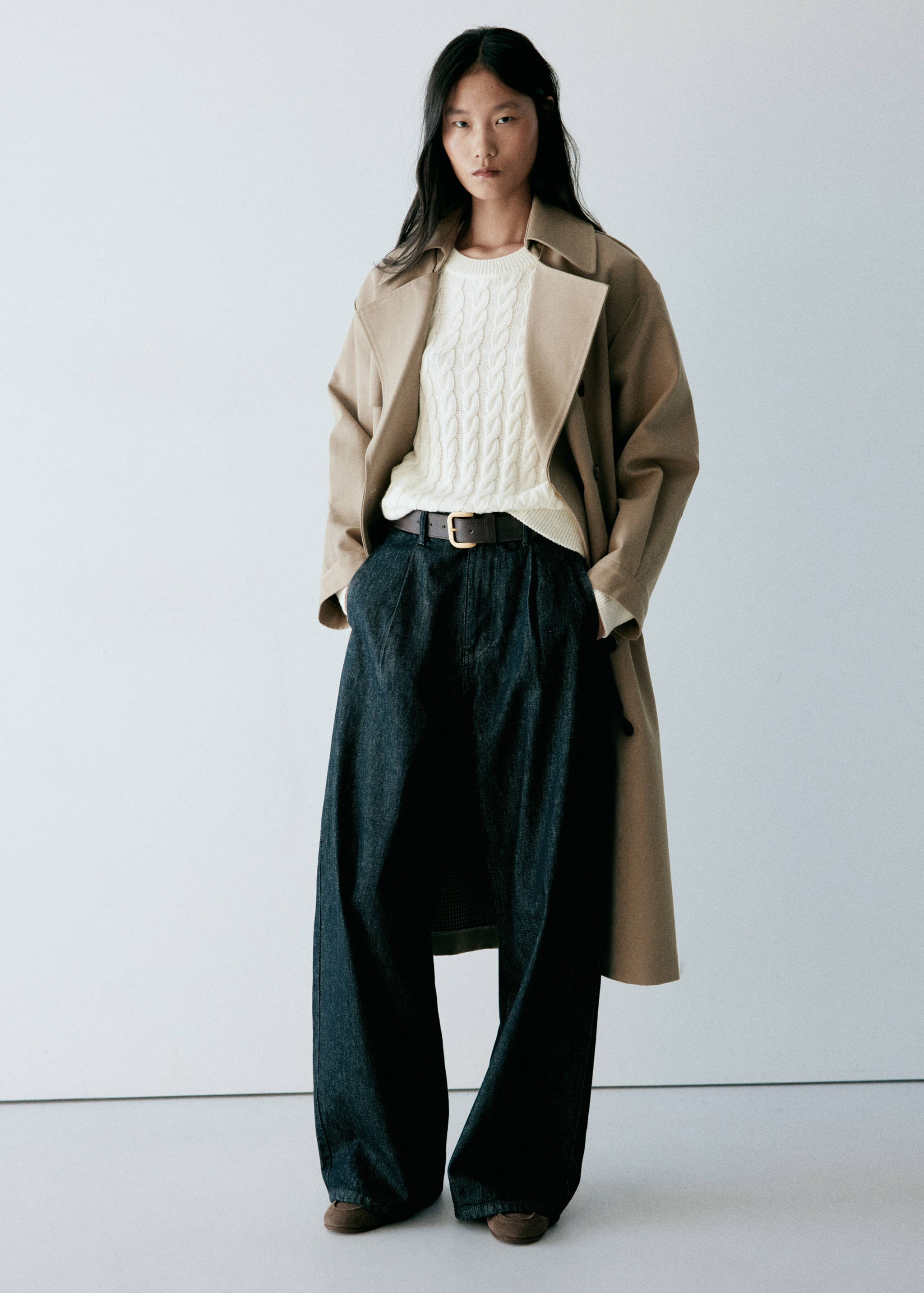 White cable-knit jersey worn with a beige trench coat and dark denim trousers.
