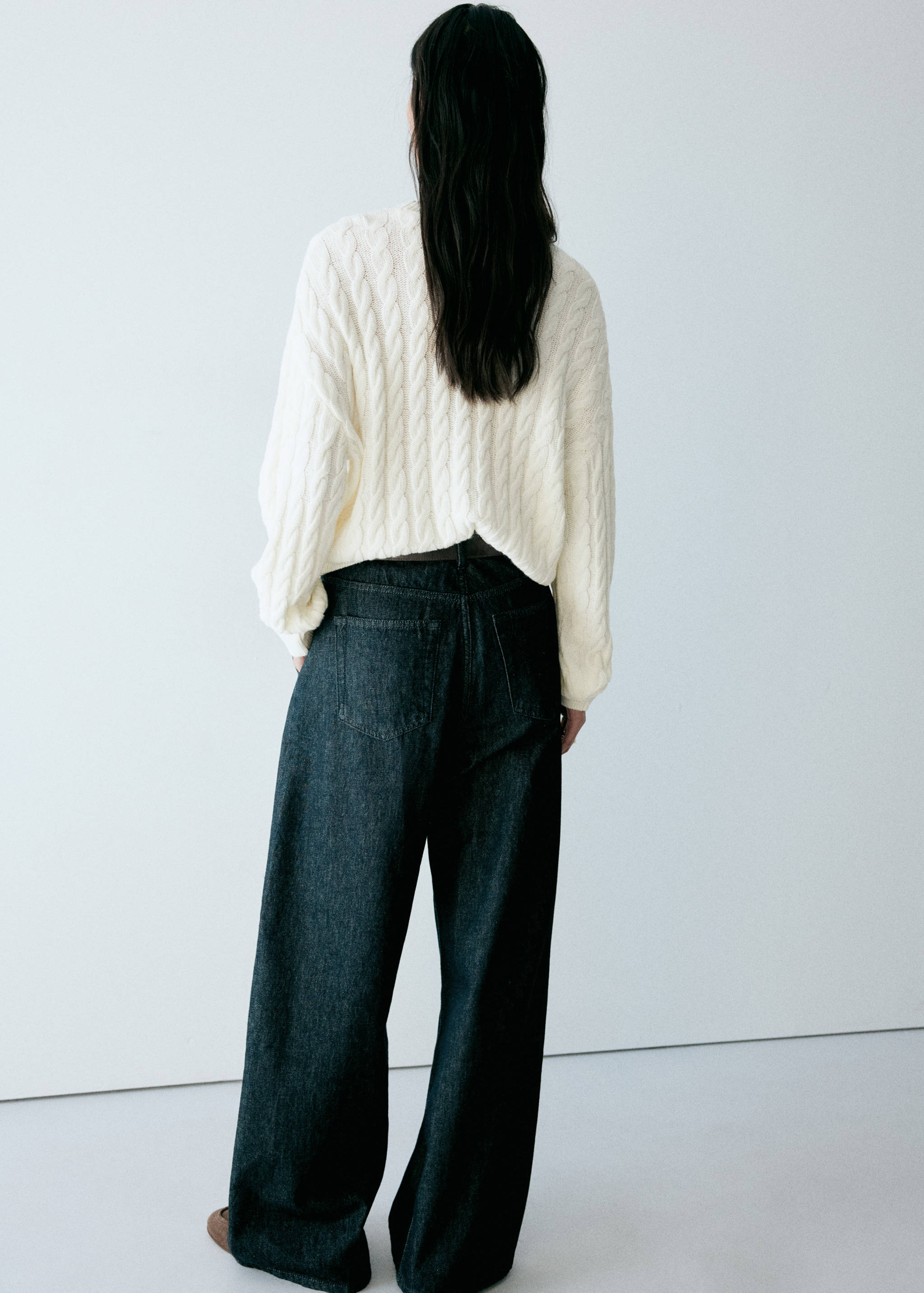 Cream white cable-knit jumper viewed from the back, worn with dark trousers.