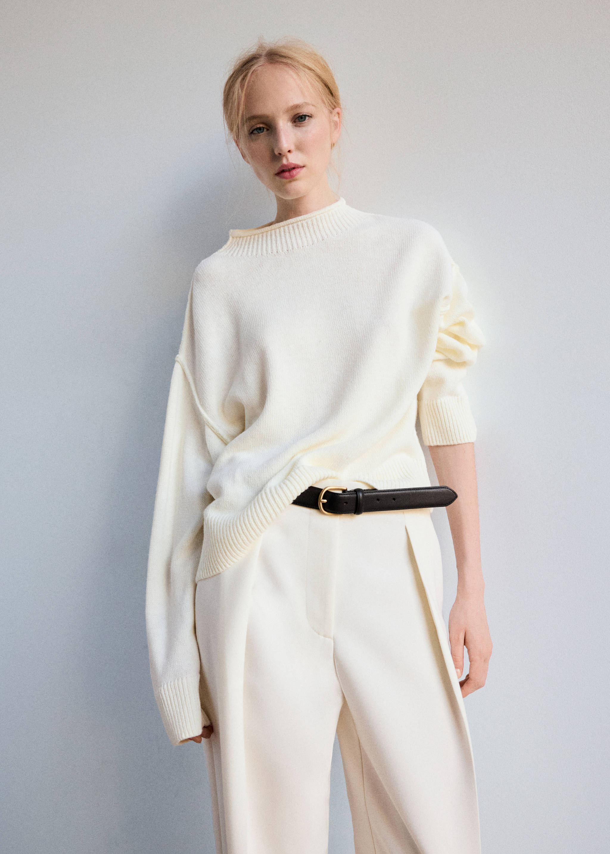 Jersey de punto en color blanco roto con cuello vuelto de canalé y hombros caídos, combinado con unos pantalones en color crema.