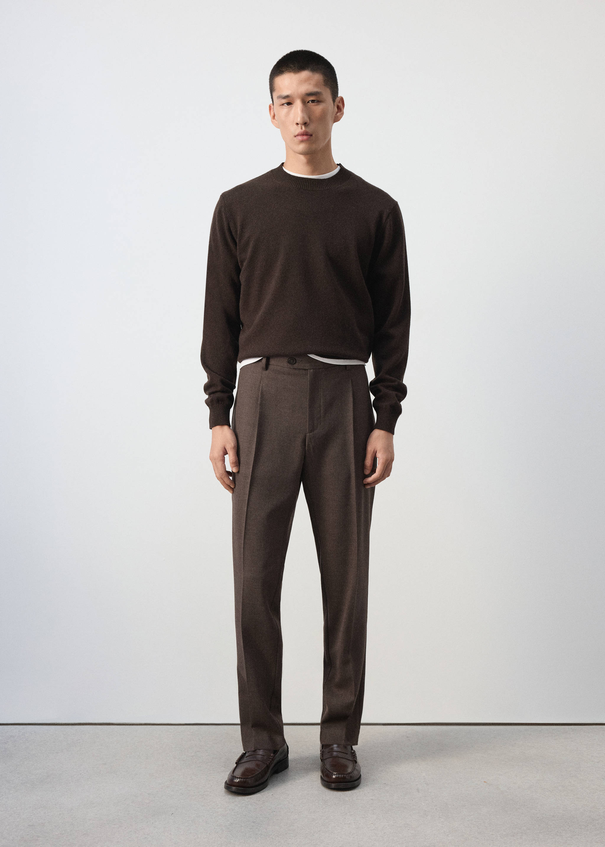 Pantalón marrón con raya marcada, combinado con un jersey de cuello redondo en marrón oscuro.