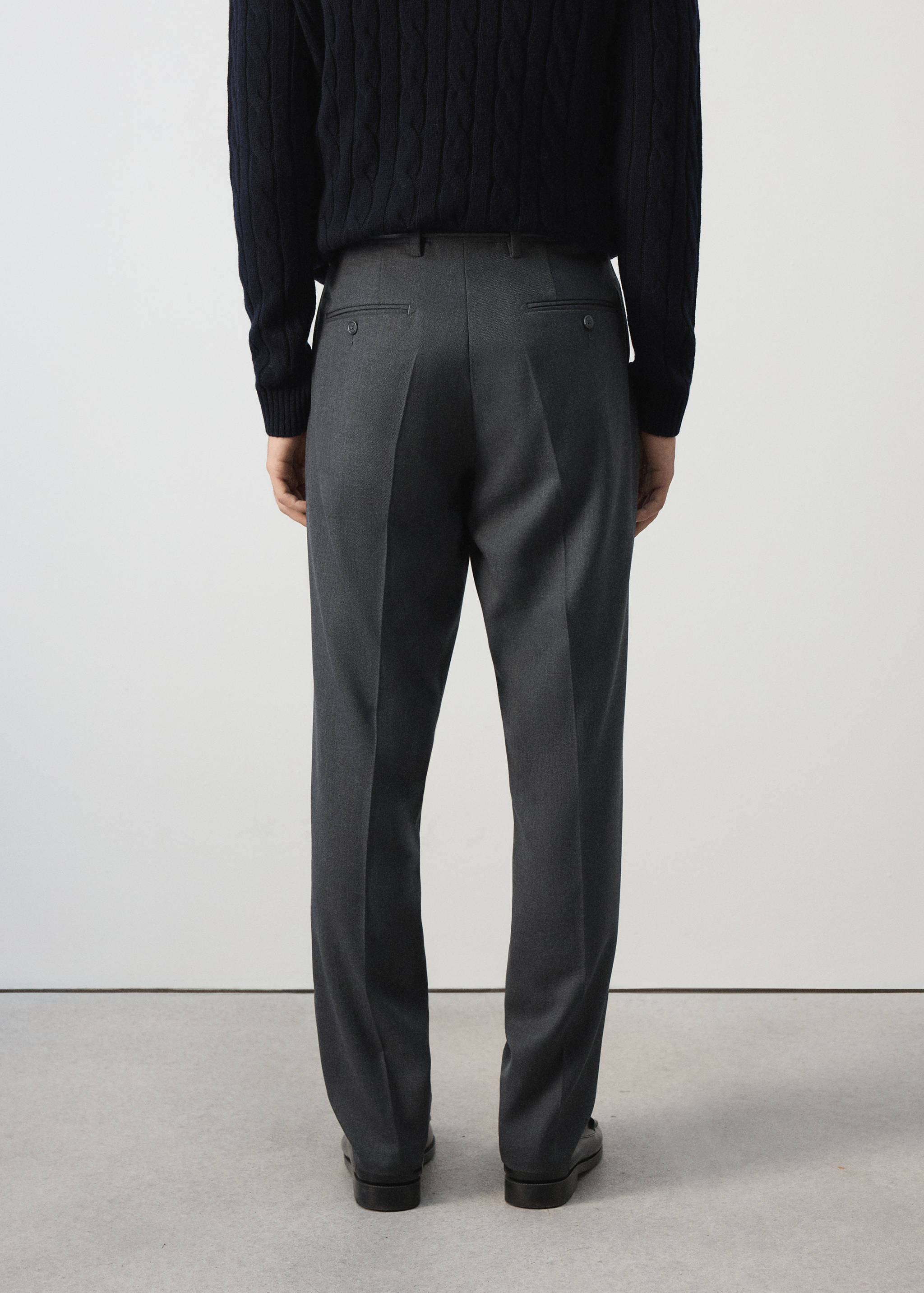 Pantalón gris oscuro, vista trasera, de diseño recto y sastre con trabillas y bolsillos de vivo abotonados.