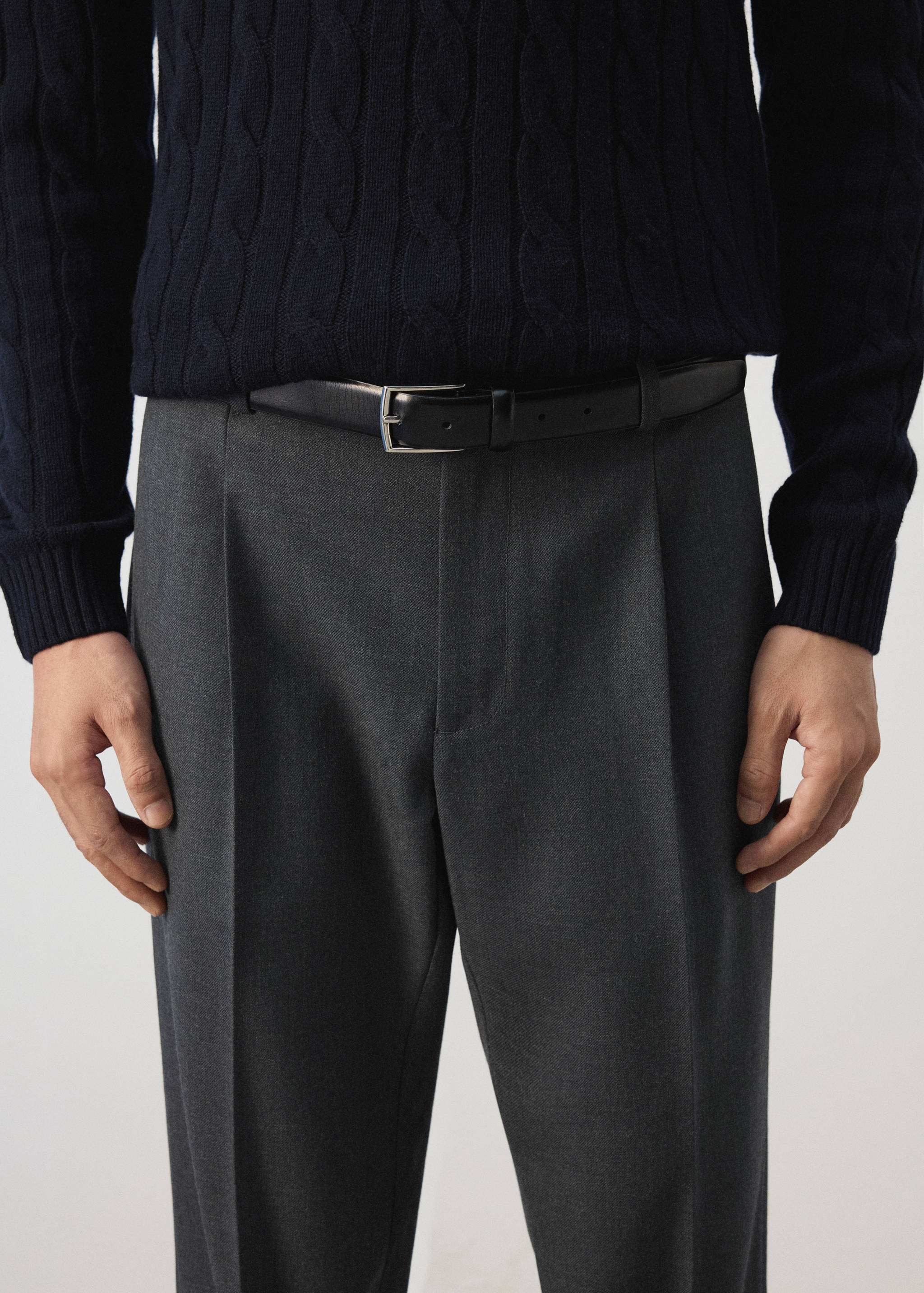 Pantalón de traje gris oscuro con pinzas y cinturón negro de piel.