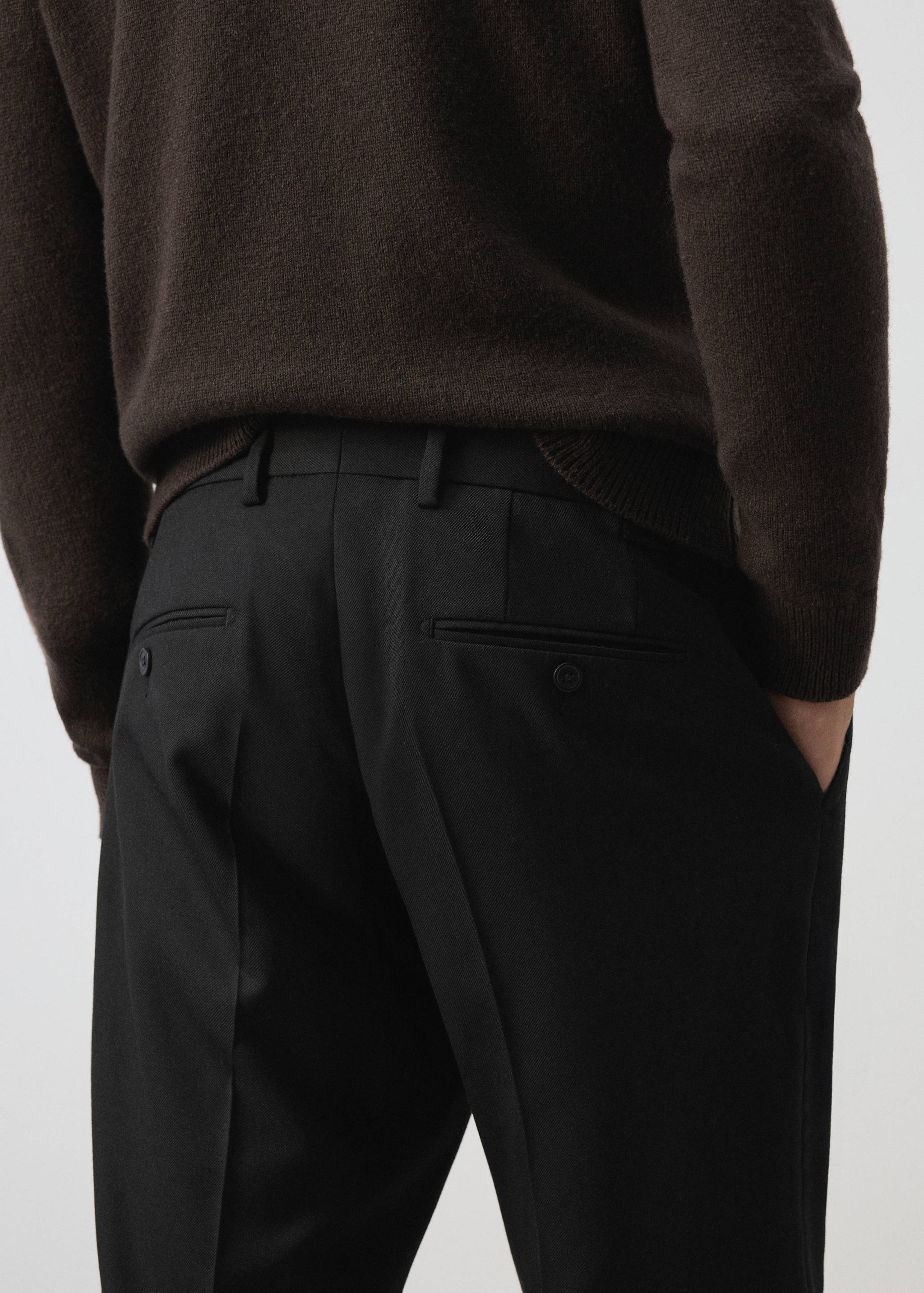 Pantalón negro con trabillas, raya planchada y bolsillos de vivo en la parte posterior, vista trasera.